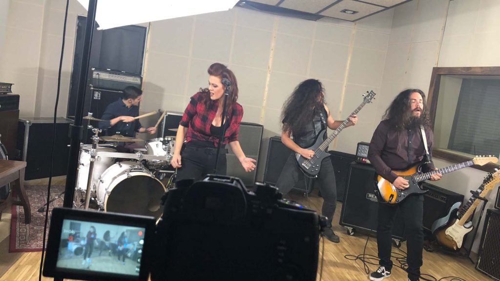 Un grupo de músicos de Metal moderno, groove metal, metalcore y deathcore tocando en un estudio de grabación en Madrid, con una mujer peliroja con apariencia agresiva en el centro, guitarra eléctrica, y varios instrumentos alrededor.