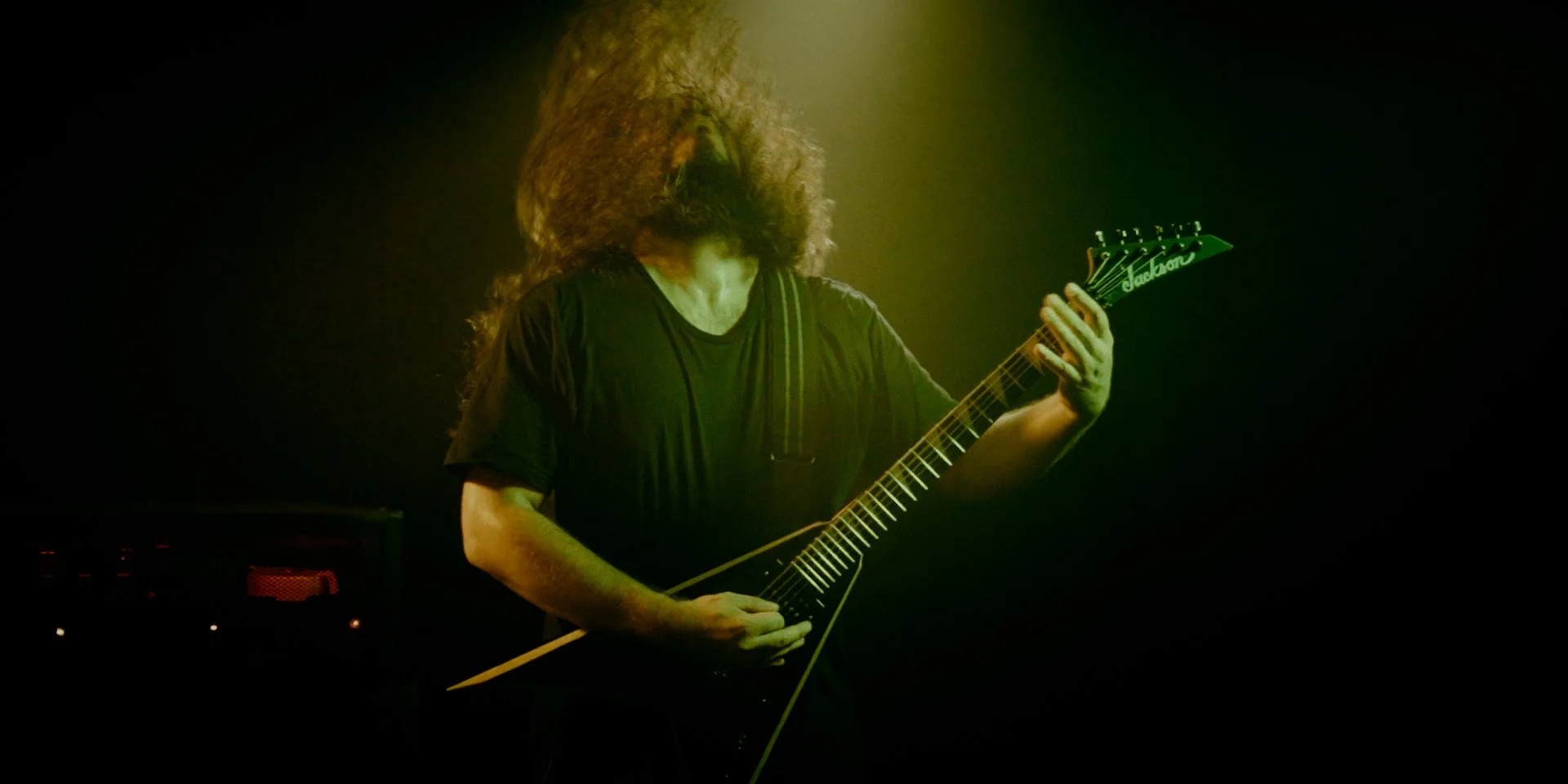 Hombre tocando Metal moderno, groove metal, metalcore y deathcore en guitarra eléctrica en un escenario con luces verdes y amarillas en el rodaje del videoclip Martillo de las brujas de Rabia Perez en Madrid