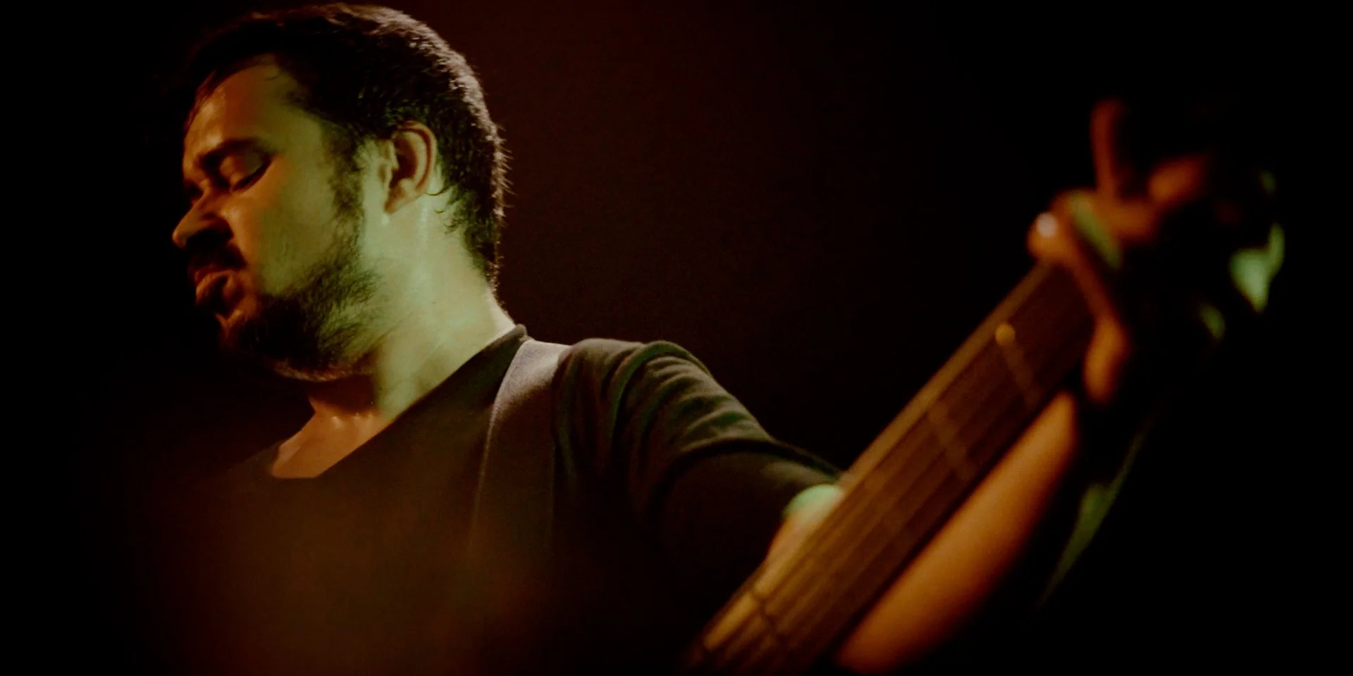 Hombre con barba tocando Metal moderno, groove metal, metalcore y deathcore en un bajo electrico en un ambiente oscuro durante el rodaje de la banda de madrid Rabia Perez.