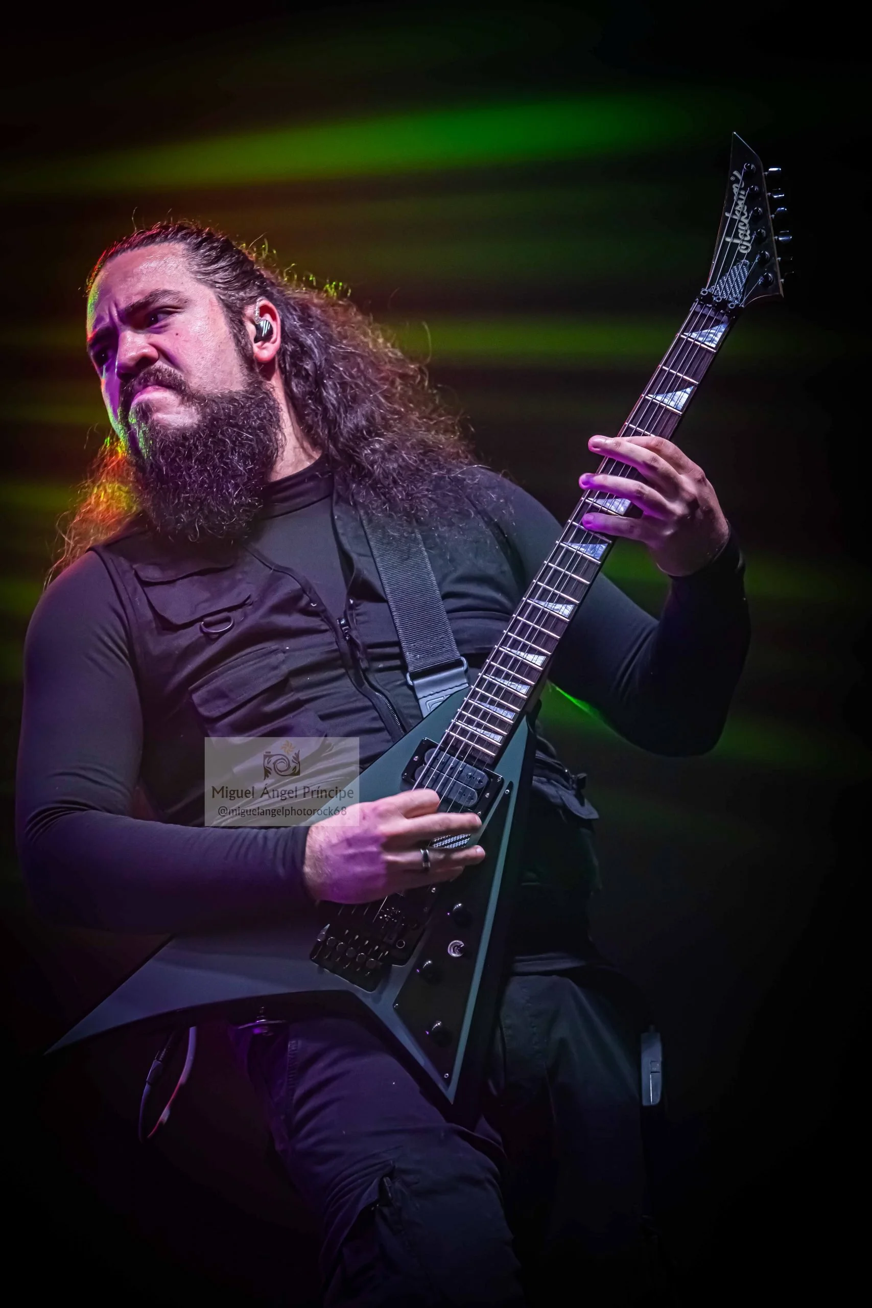 Hombre fundador de la banda de Madrid de Metal moderno, groove metal, metalcore y deathcore tocando guitarra eléctrica en un escenario con luces de color verde y amarillo.