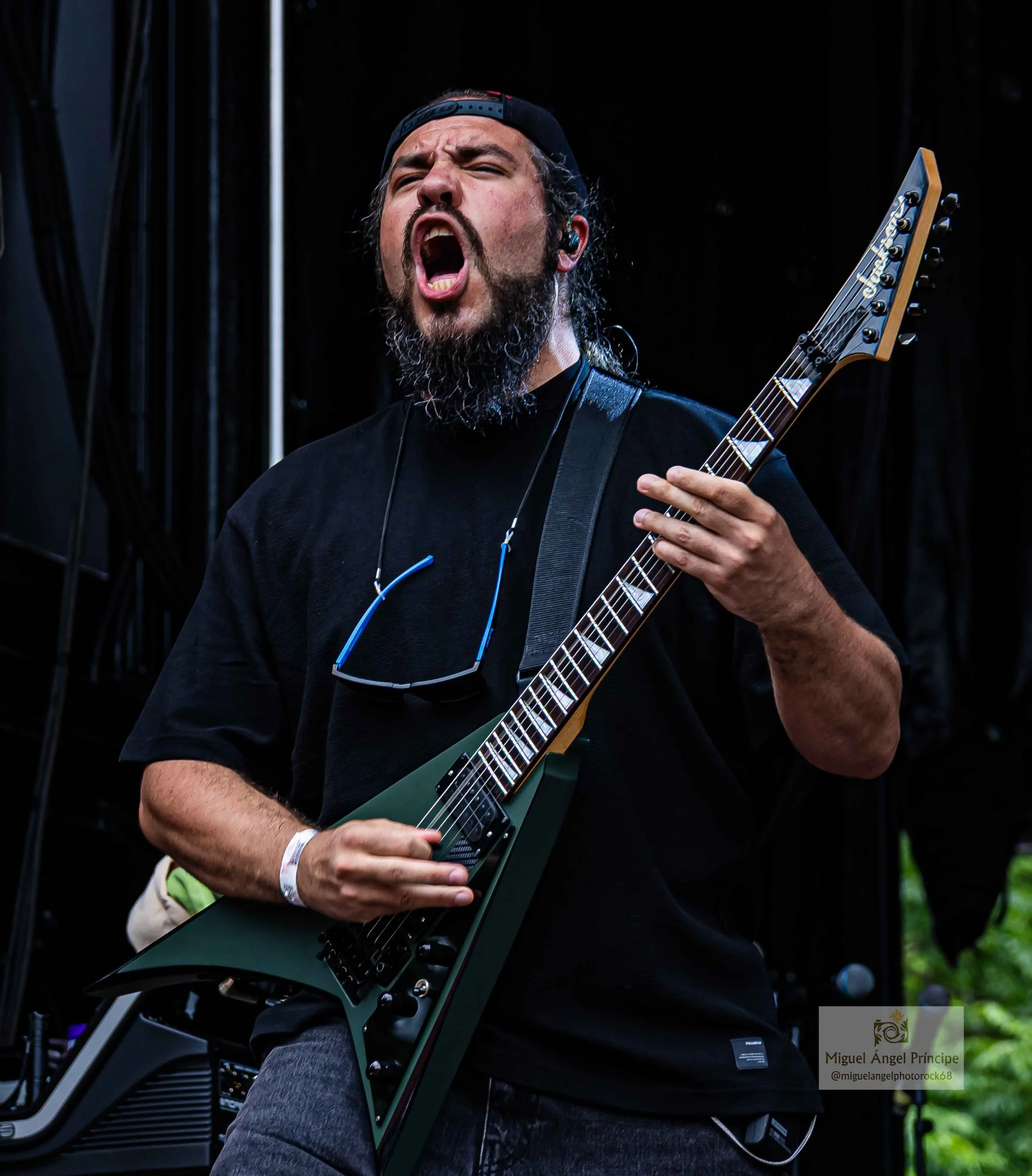 Hombre fundador de la banda de madrid de Metal moderno, groove metal, metalcore y deathcore con barba tocando guitarra eléctrica en concierto. Tiene gorra y está en escenario.