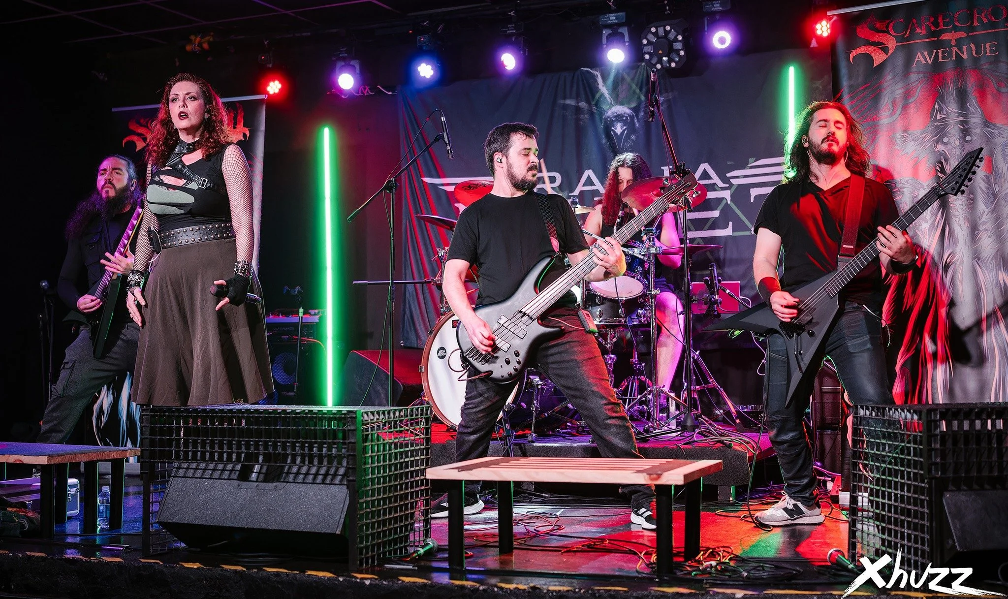 Una banda de Metal moderno, groove metal, metalcore y deathcore cinco músicos en un escenario durante un concierto, con instrumentos eléctricos, luces de colores y una cortina con logotipo y arte de fondo.