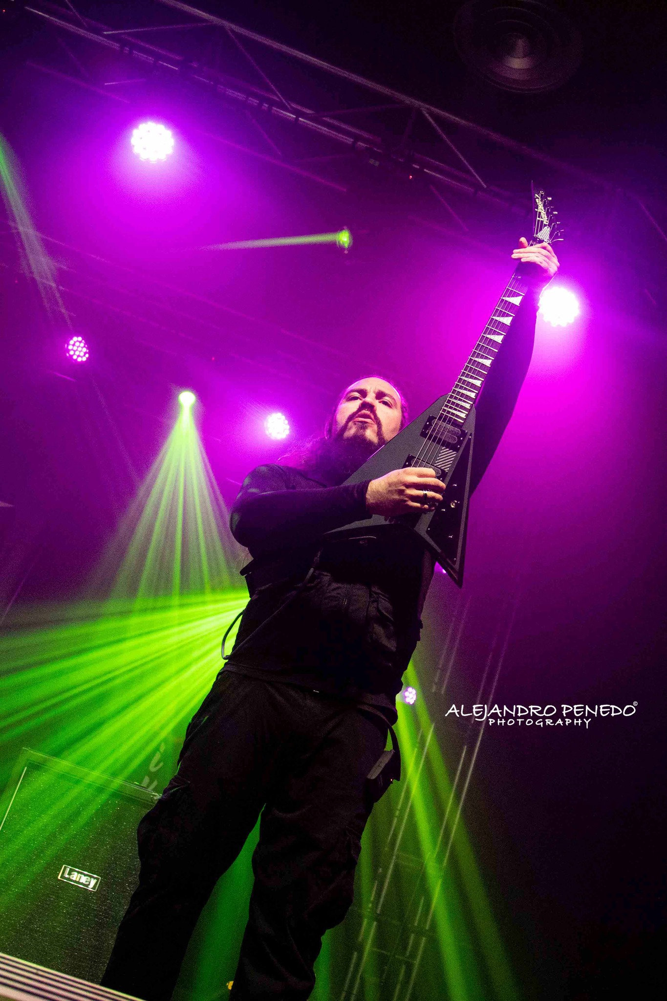 Hombre tocando Metal moderno, groove metal, metalcore y deathcore en una guitarra eléctrica Jackson en concierto, rodeado de luces moradas y verdes en Madrid.