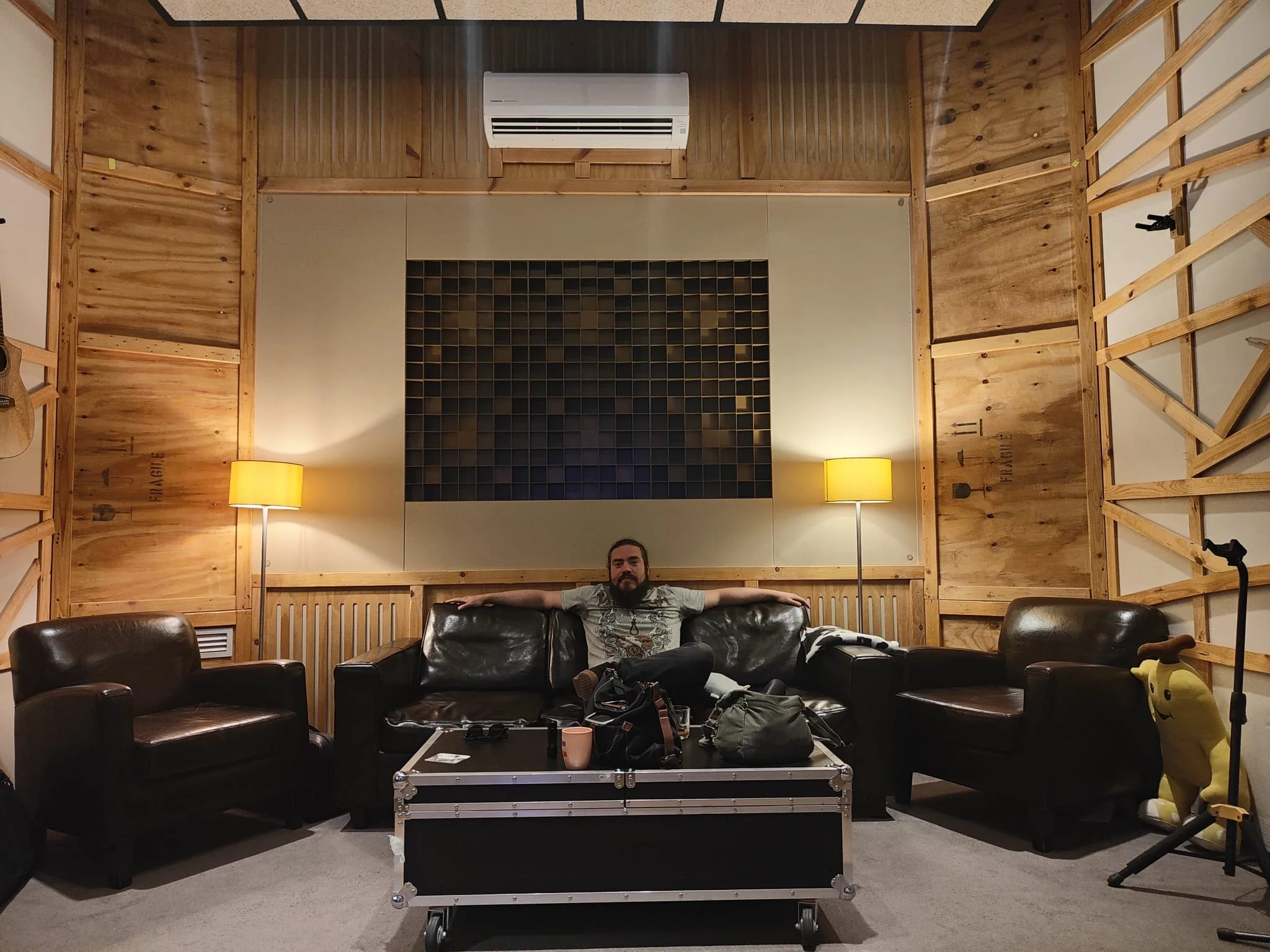 Madrid. Metal moderno, metalcore, Groove metal y deathcore.Hombre sentado en un sofá de piel en una sala de grabación con paredes de madera, lámparas de pie encendidas y equipo de grabación sobre una mesa