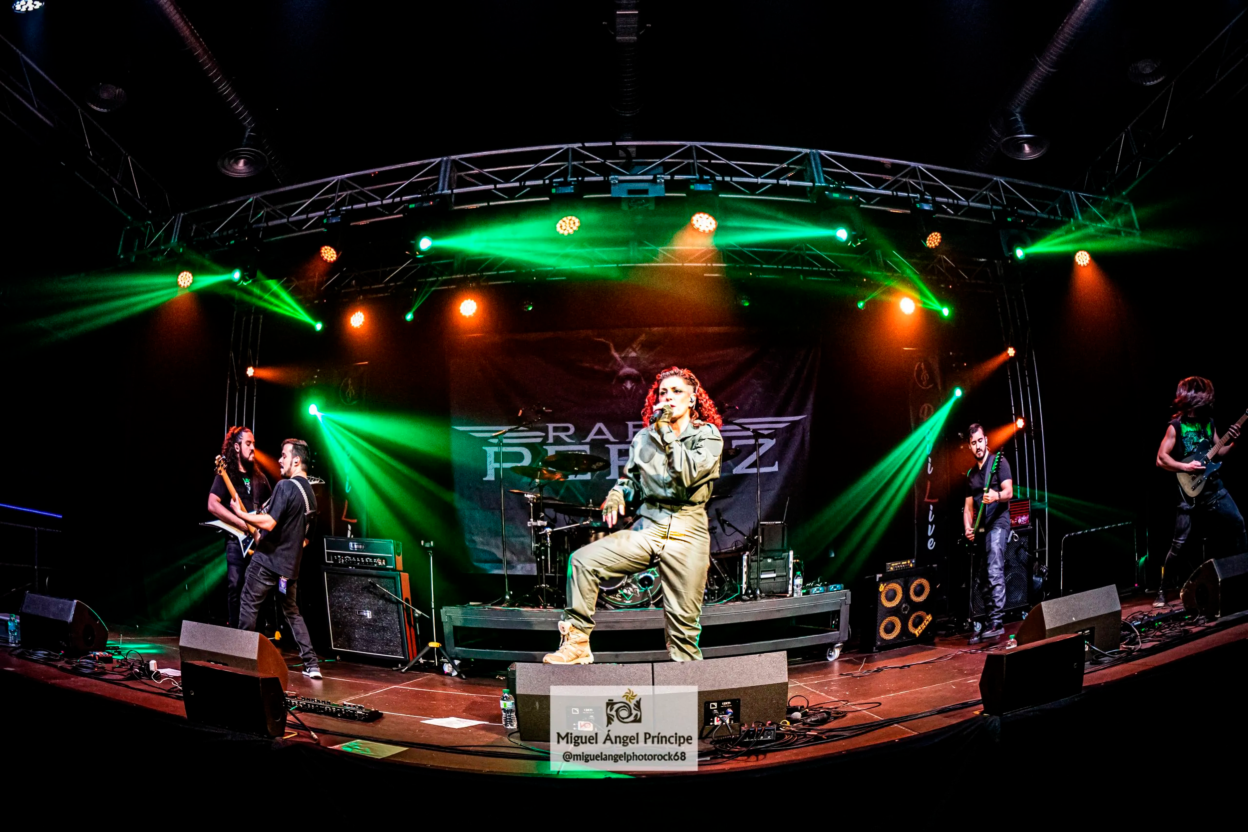 Concierto en Madrid en vivo con banda de Metal moderno, groove metal, metalcore y deathcore Rabia Perez tocando en escenario con luces verdes y naranjas, y una cantante en el centro con micrófono.