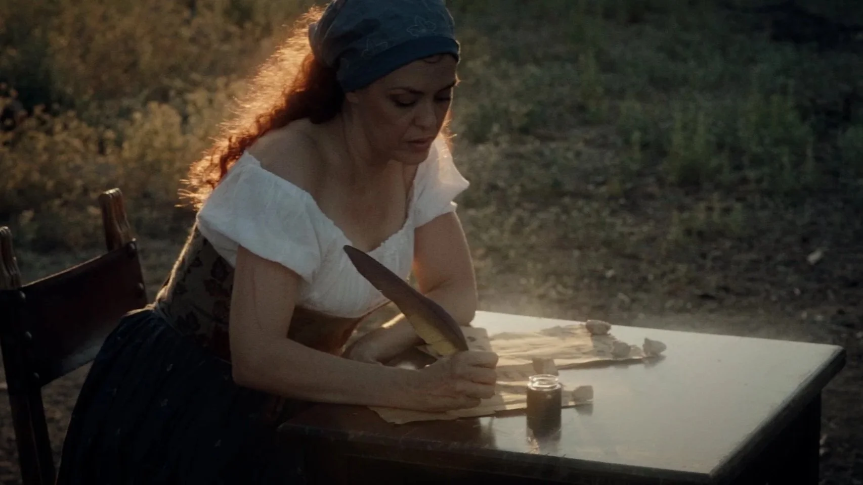 Mujer con pañuelo en la cabeza trabajando con papel y tinta en un asiento exterior en un entorno natural durante el rodaje de videoclip de la banda de Metal moderno, groove metal, metalcore y deathcore de madrid Rabia Perez.
