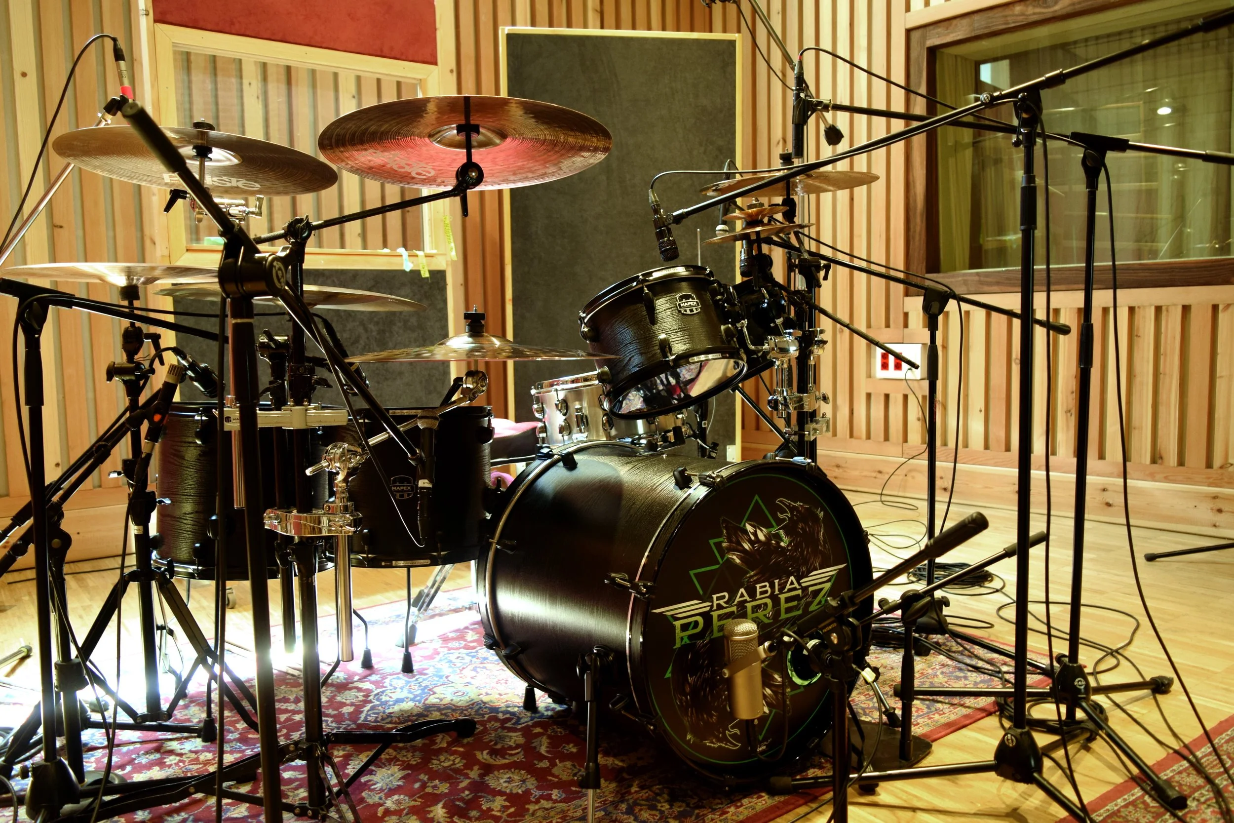 Batería de estudio en una cabina de grabación con paravientos y micrófonos.