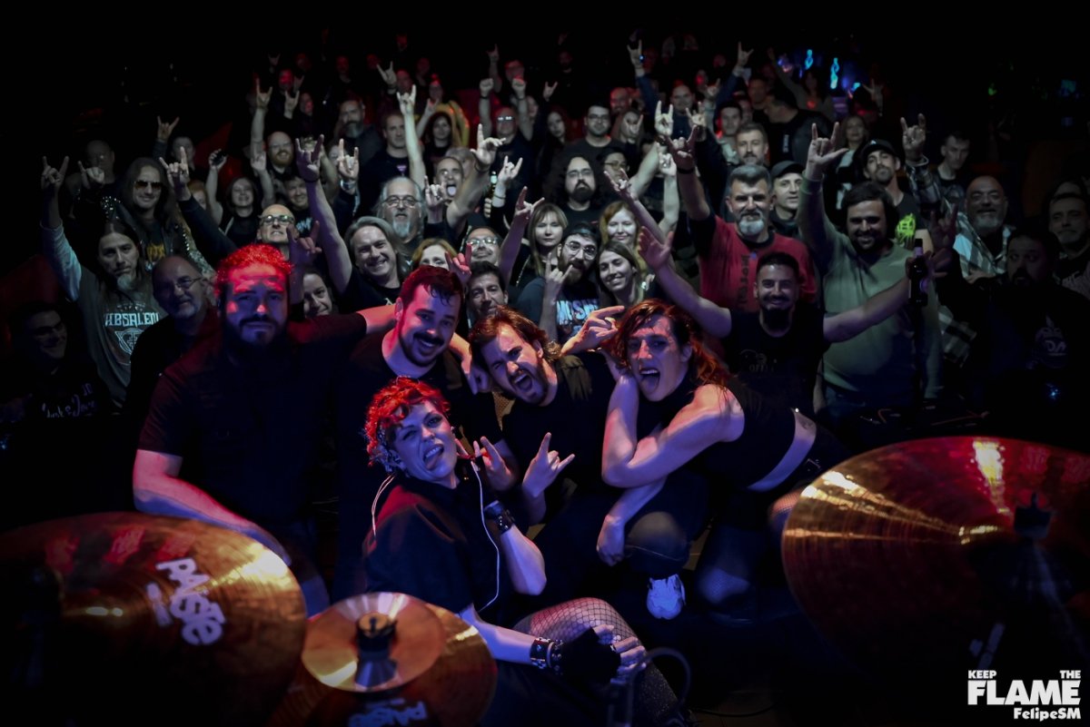 Un grupo de personas en un concierto o evento, posando para la cámara y haciendo gestos de rock, en un ambiente oscuro con iluminación colorida.