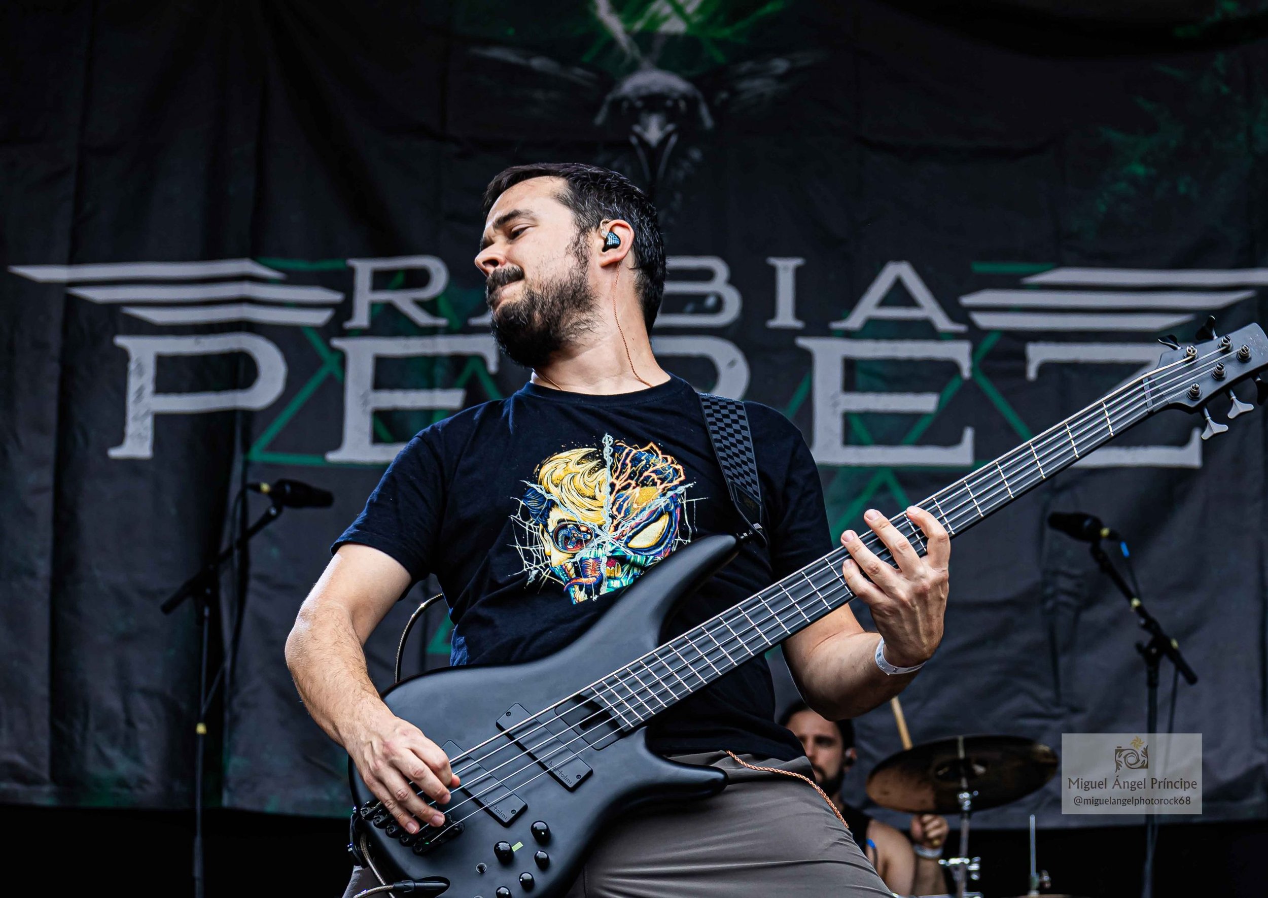 Un hombre tocando Metal moderno, groove metal, metalcore y deathcore en un bajo electrico en un escenario durante un concierto, con fondo que dice 'RABIA PEREZ' banda de Madrid.