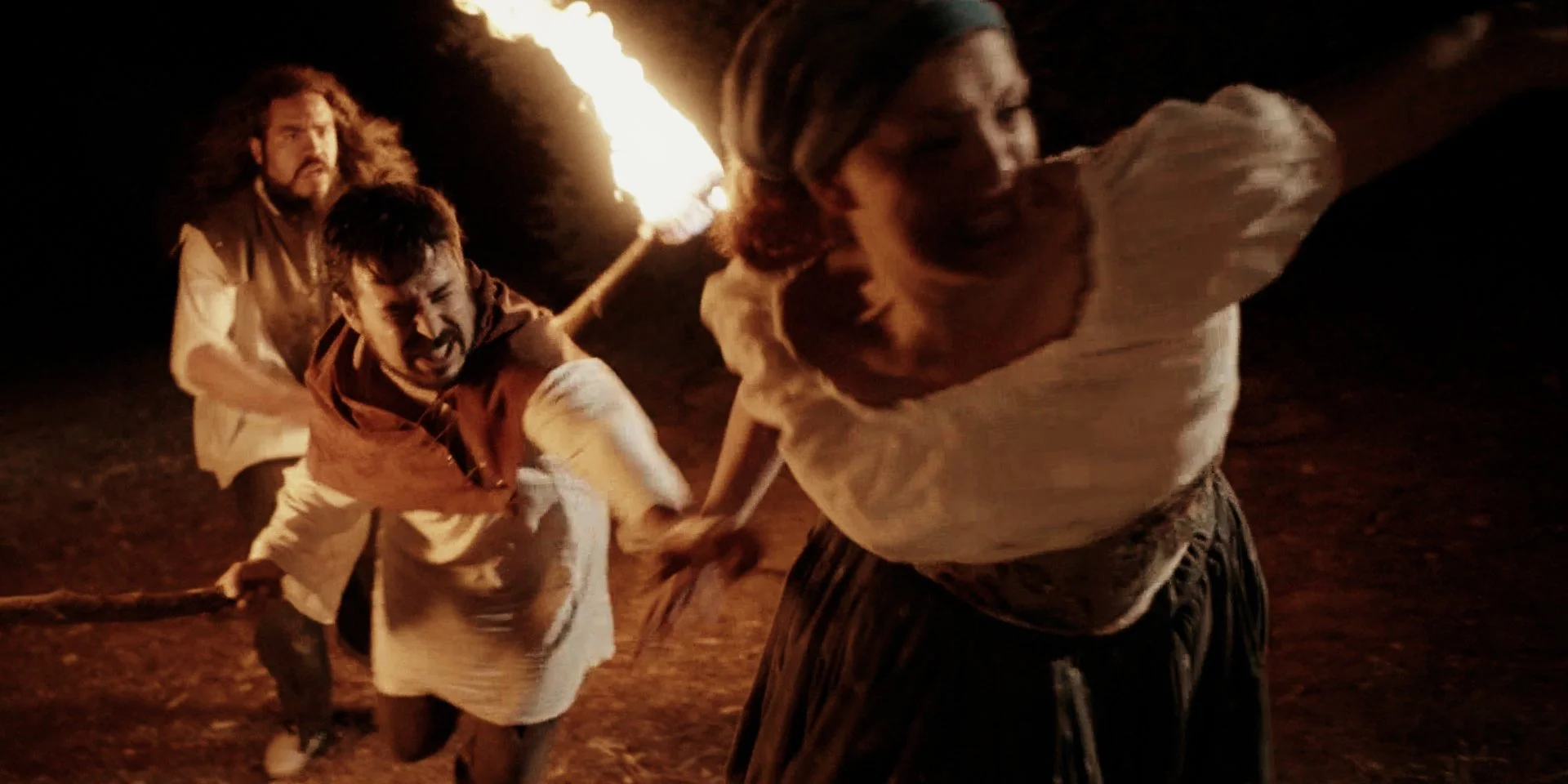 Tres personas corriendo en la noche con una antorcha de fuego, expresando miedo o angustia.