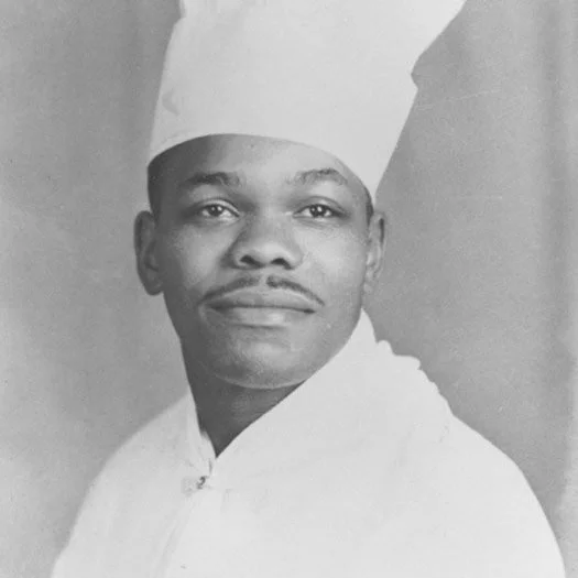 Black and white portrait of a man wearing a chef's hat and white chef's uniform.