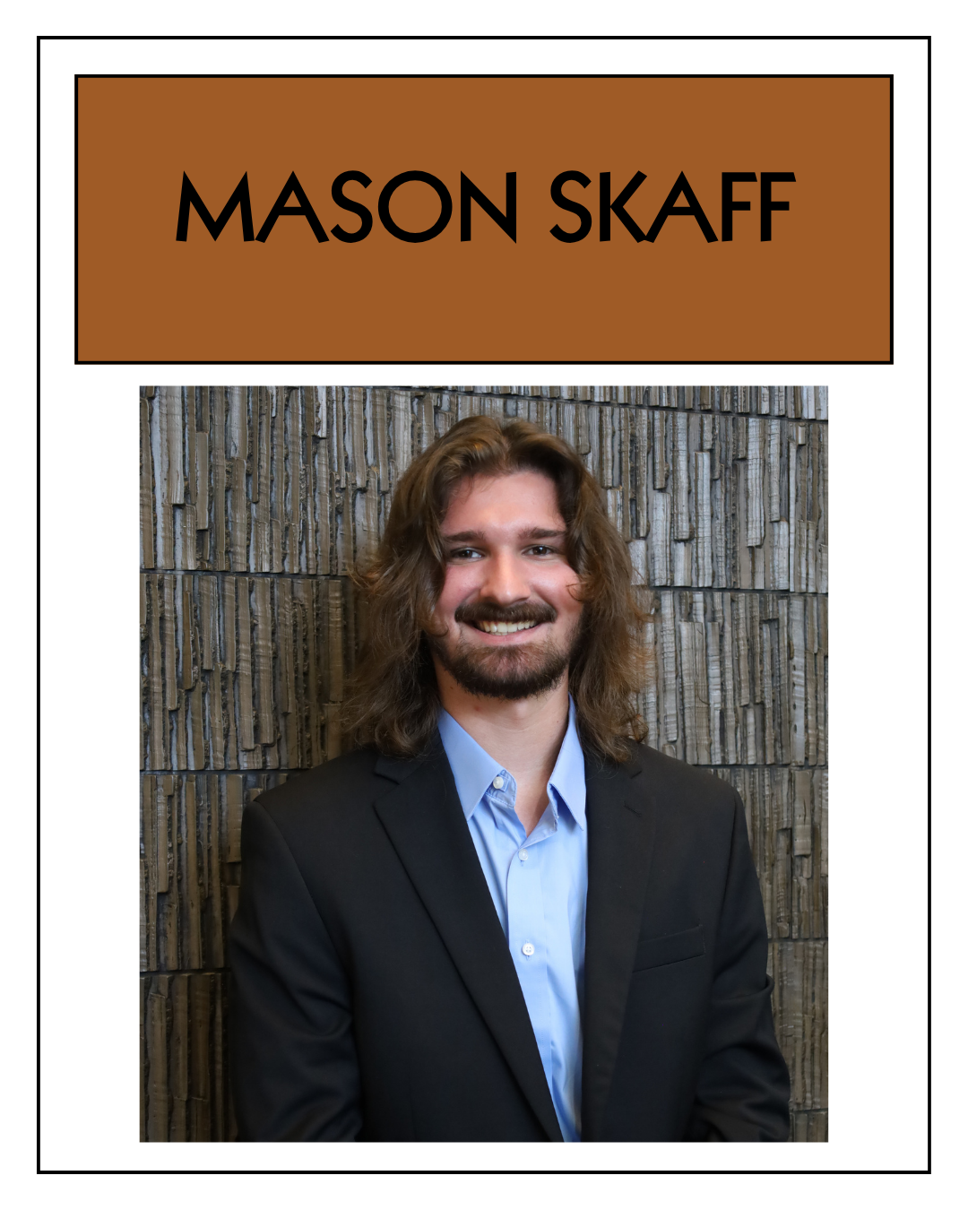 A professional portrait of Mason Skaff with long, wavy hair, beard, wearing a black suit and light blue shirt, standing against a textured brick wall.