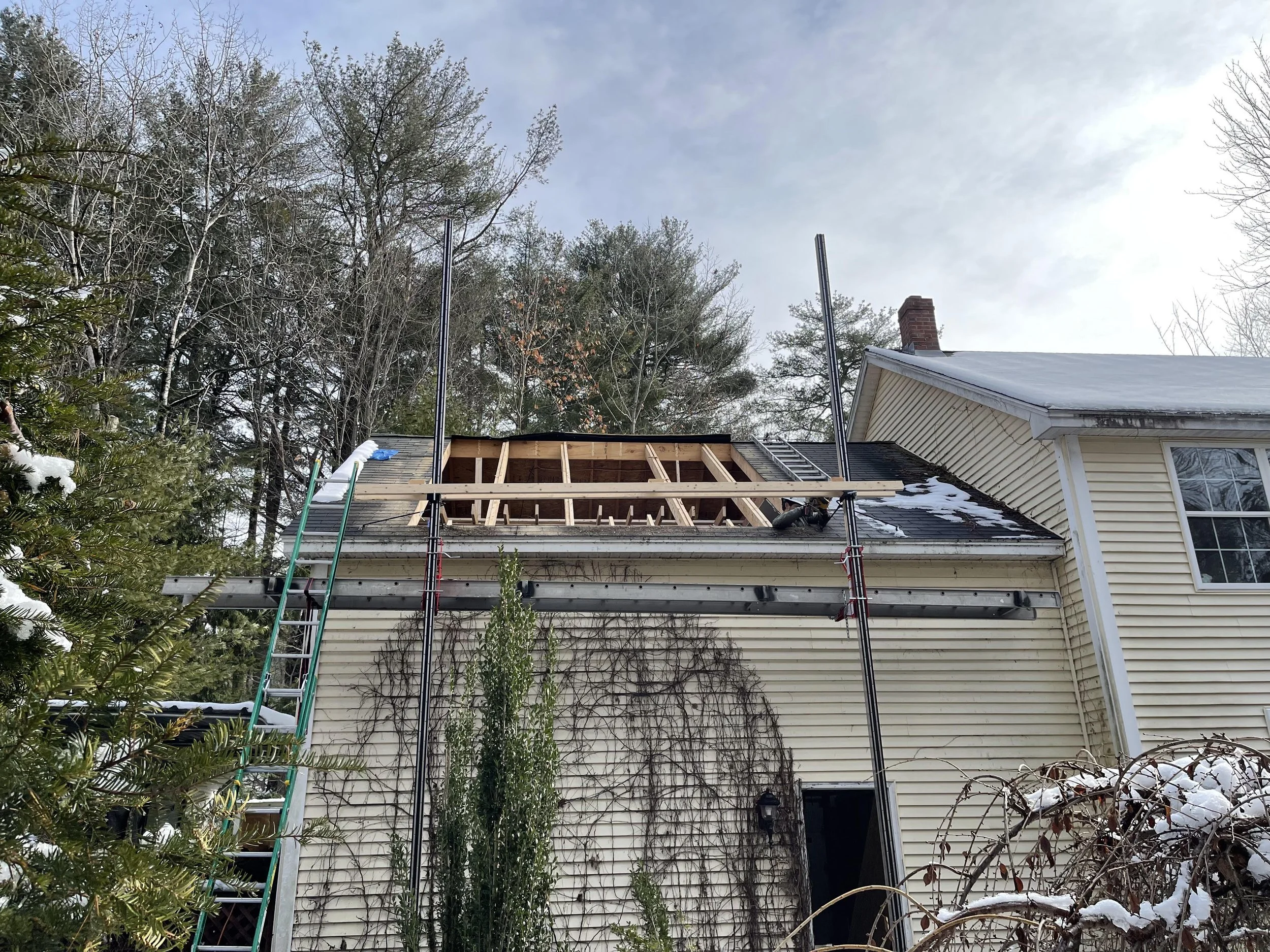 Construction work on a house roof, with a new wooden frame being built and scaffolding in place, on a snowy winter day.