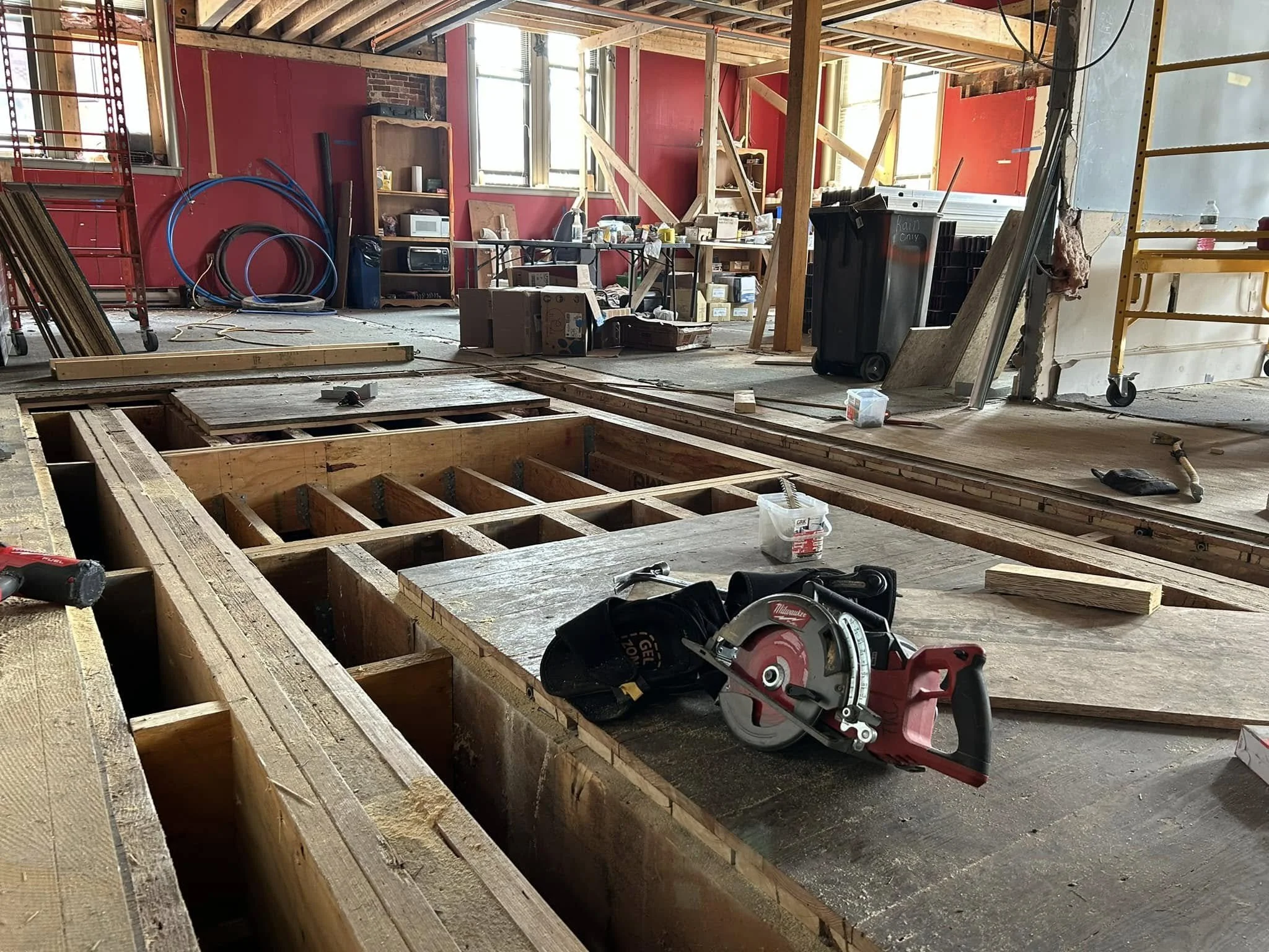 Interior of a house under renovation with exposed wooden framing, construction tools, and supplies scattered around.