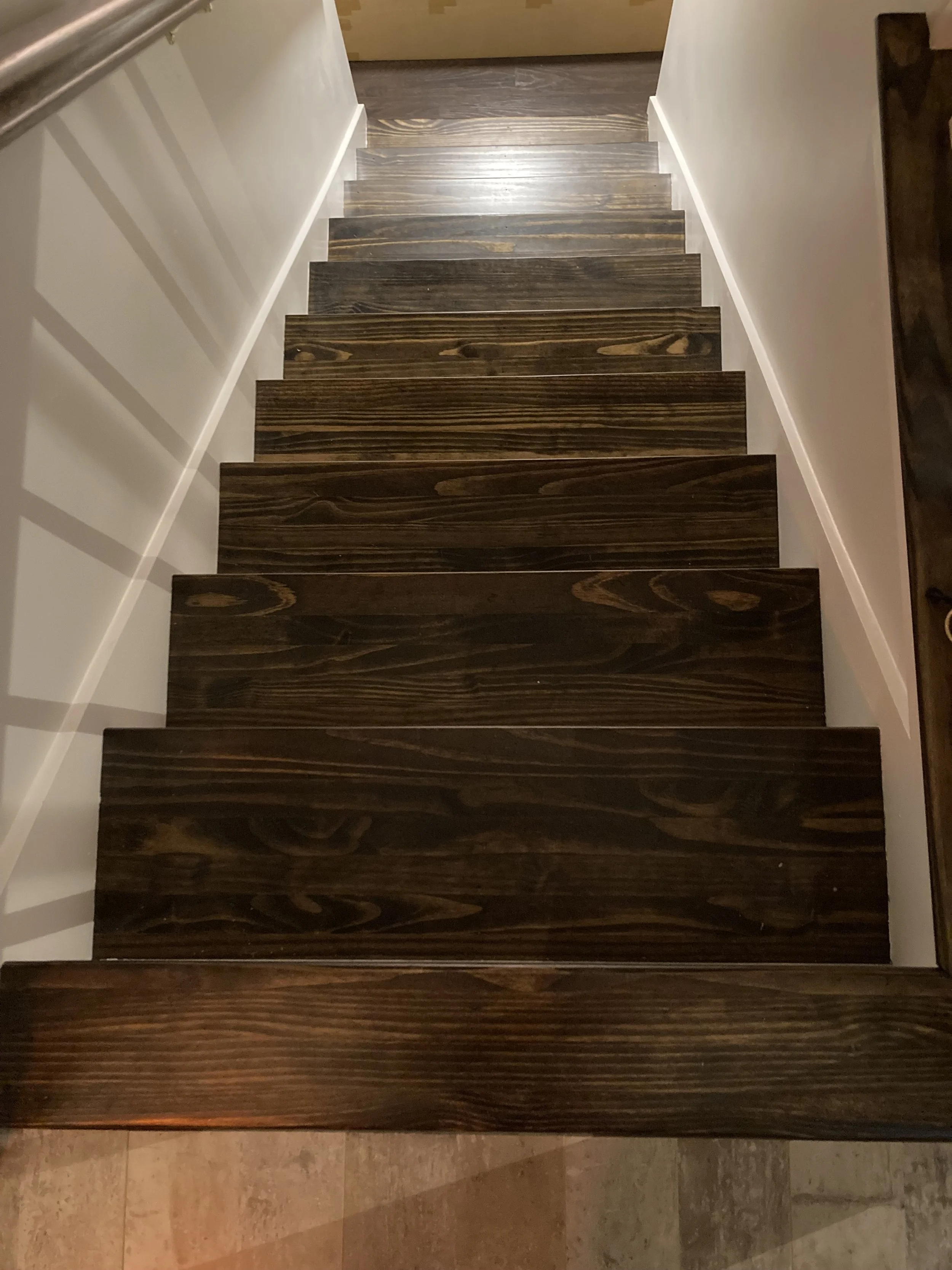 Dark wooden stairs viewed from above, with white walls on either side.