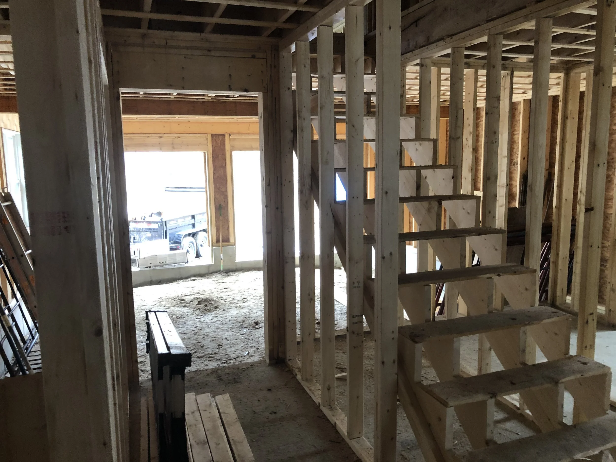 Interior view of a house under construction, showing wooden framing, staircase, and unfinished walls.