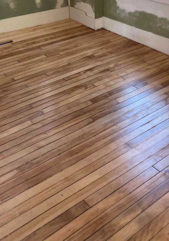 A corner of a room with newly installed wooden flooring and unfinished walls.