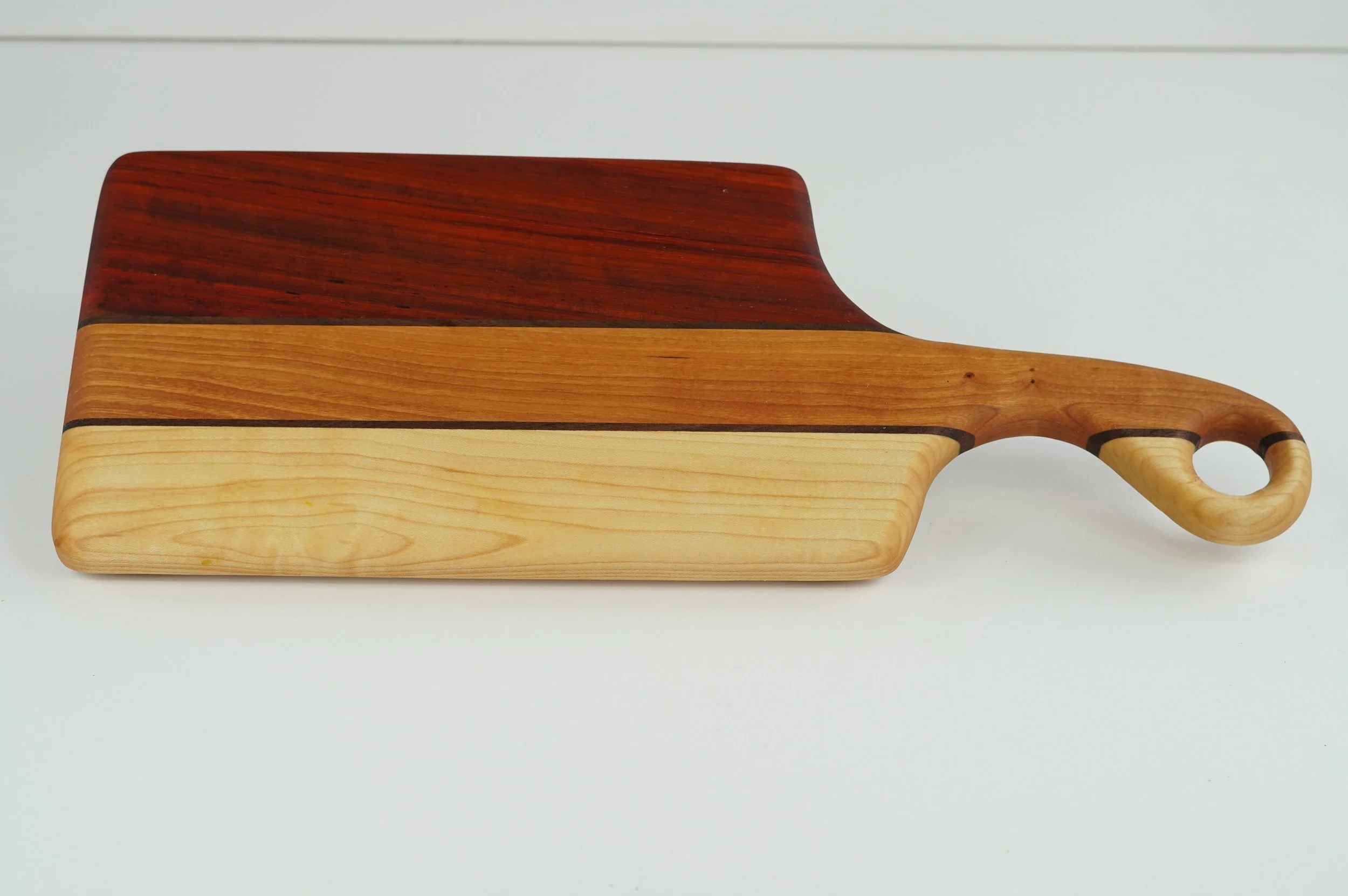 Small cutting and charcuterie board made from Padauk, Cherry, Hard Maple, and Walnut with a striped hardwood pattern.