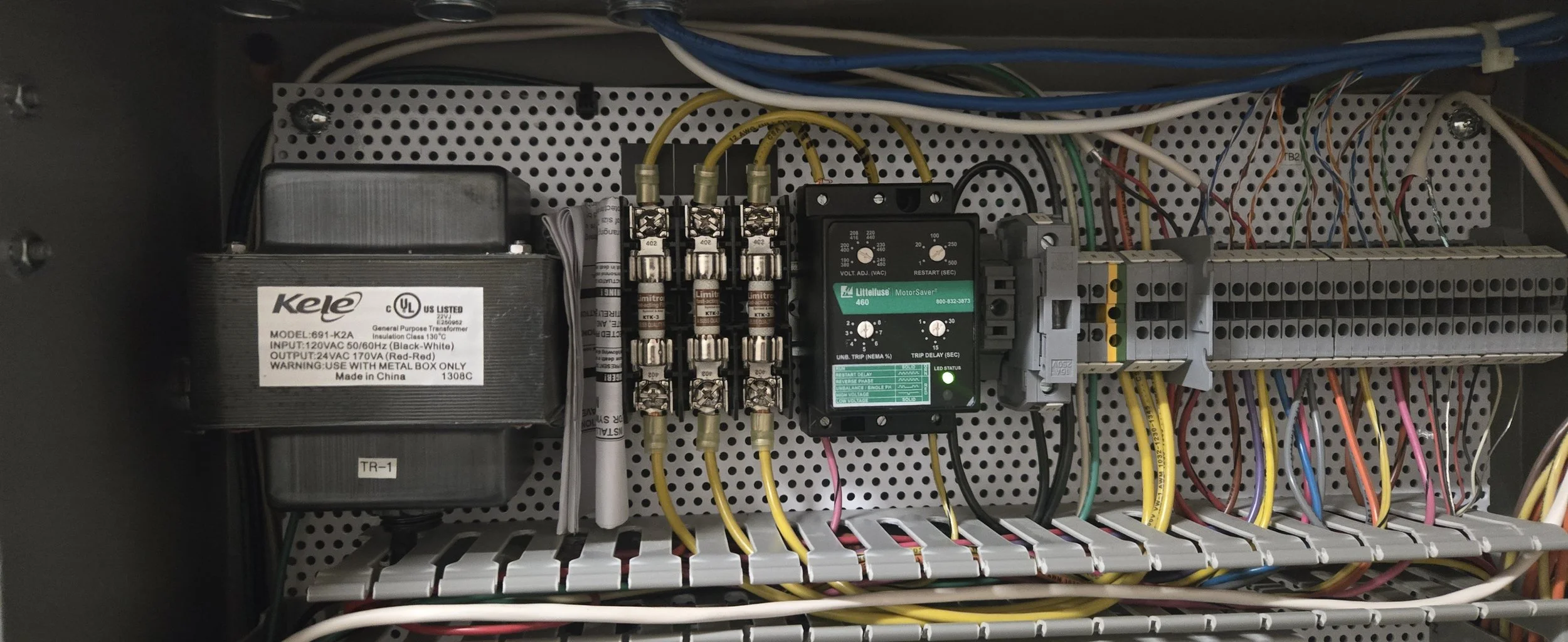 Electrical control panel with circuit breakers, transformers, relays, wiring, and a motor controller mounted on a perforated metal backplate.