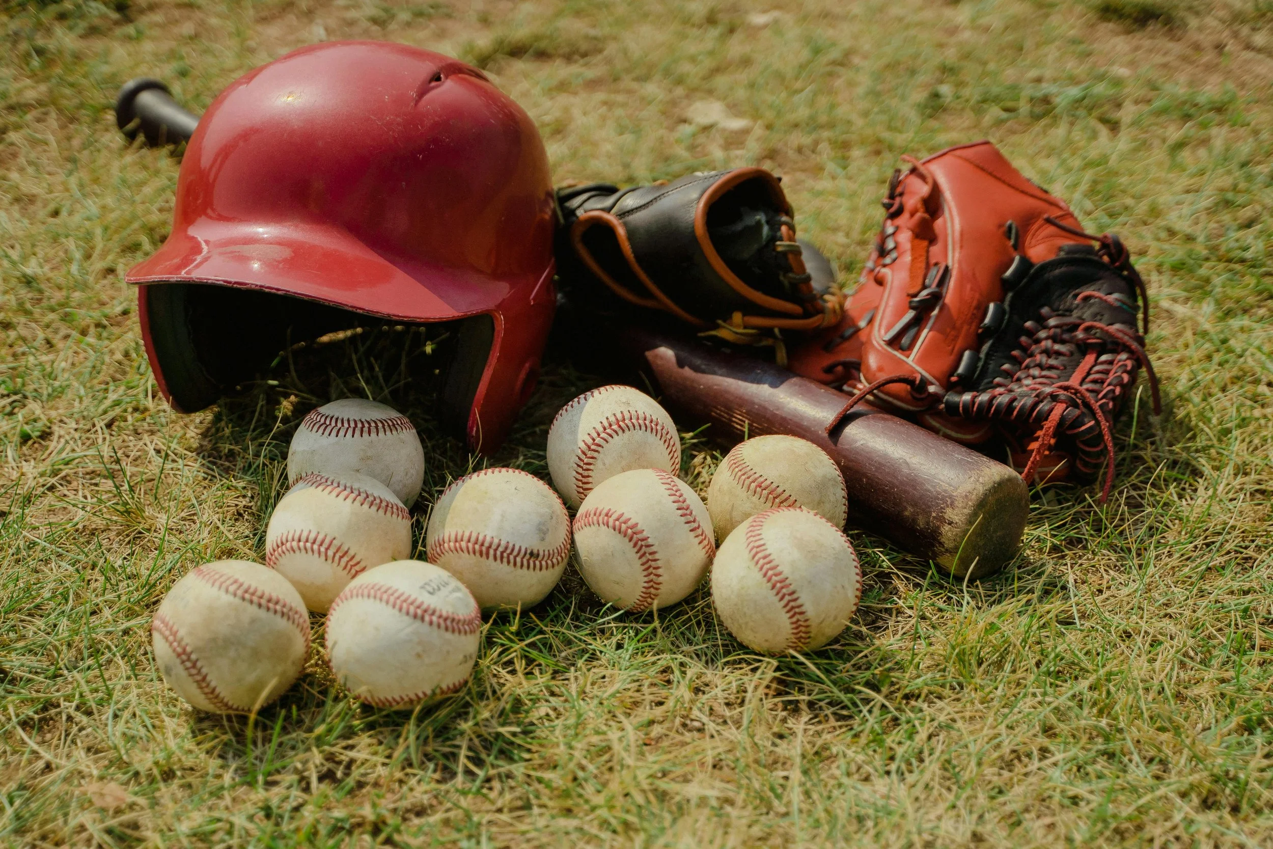 Baseball helmet, glove, bat, and multiple baseballs on grass field.