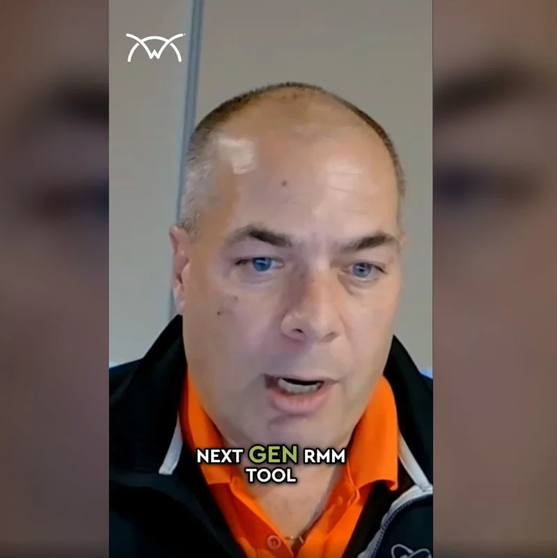 A man with a shaved head and light skin, wearing a black jacket with orange underneath, is speaking and looking slightly off-camera. There are subtitles at the bottom that say, "NEXT GEN RMM TOOL."