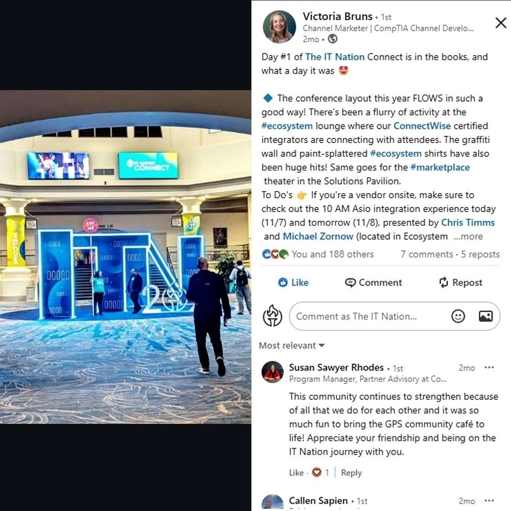 Photo of a conference entrance with large digital screens and blue booth displays, attendees walking in a spacious indoor area