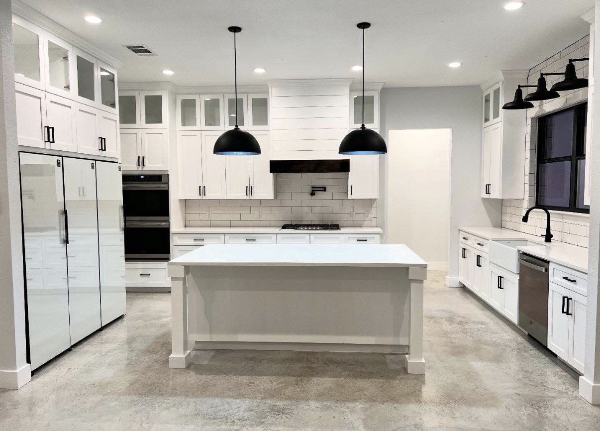 Modern white kitchen with black fixtures, a central island, stainless steel appliances, and black pendant lights hanging above the island.