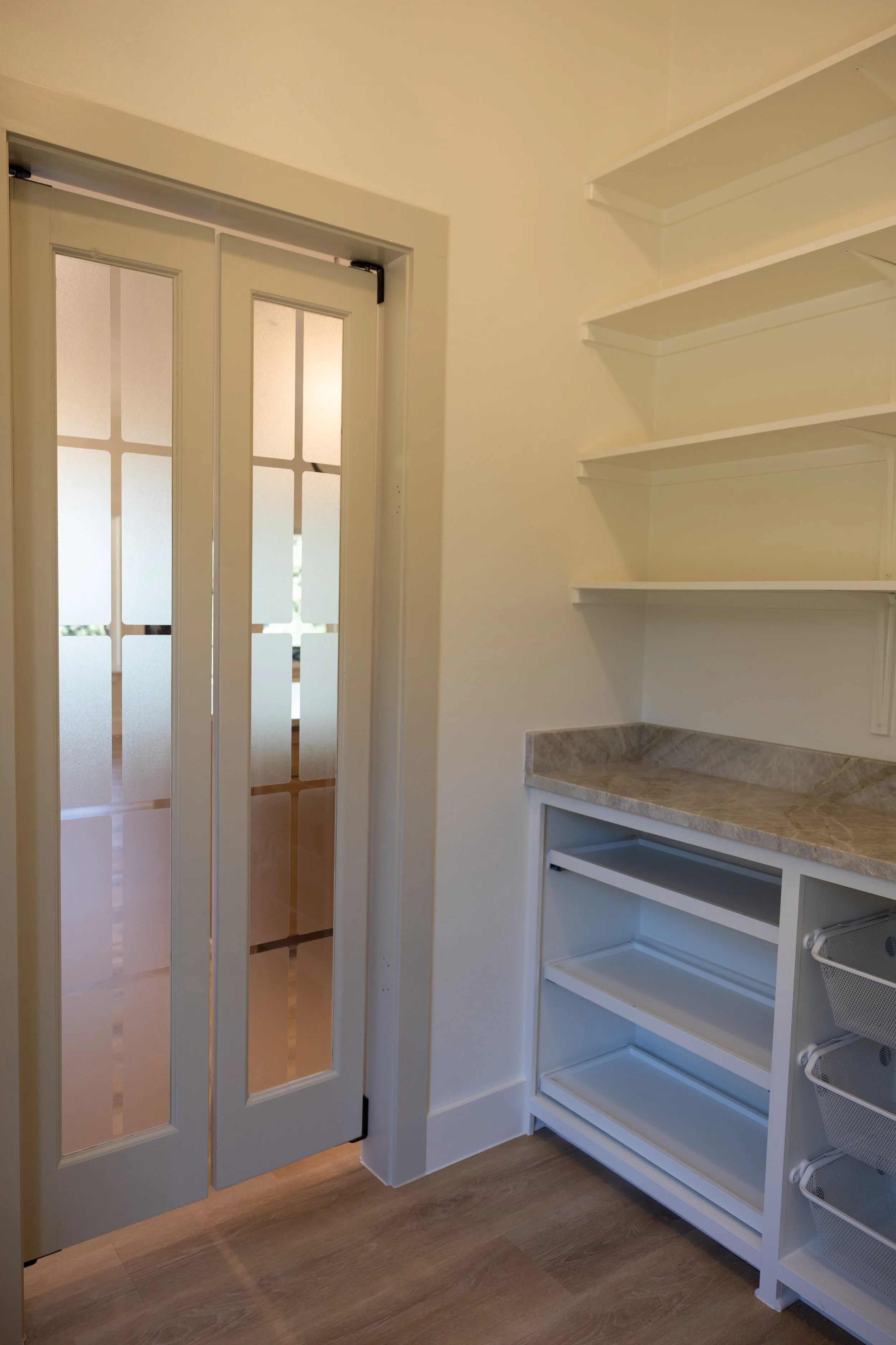 Empty kitchen or pantry with open white shelves, a marble countertop, and a door with glass panels.