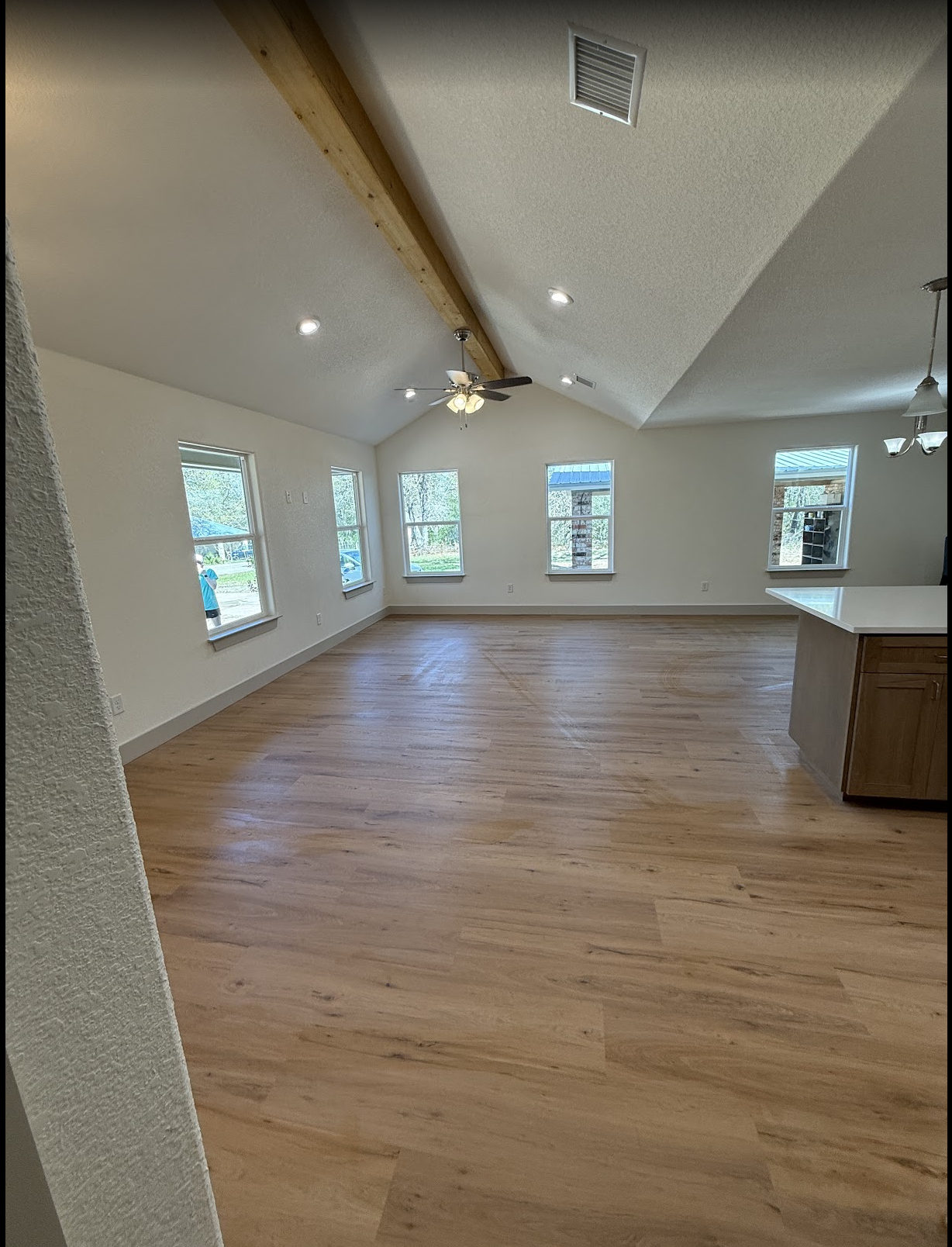 Empty living room with wooden floors, multiple windows, a ceiling fan, and a wooden beam on the ceiling.