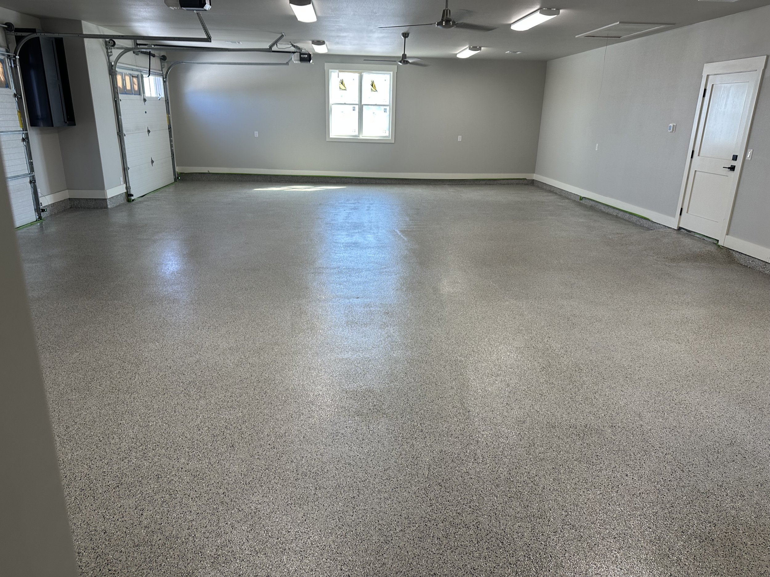 Empty garage with polished epoxy floor, white walls, a window, and a garage door.