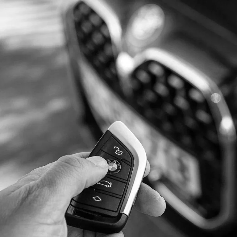 Une main tenant une clé de voiture BMW devant une grille de radiateur de voiture