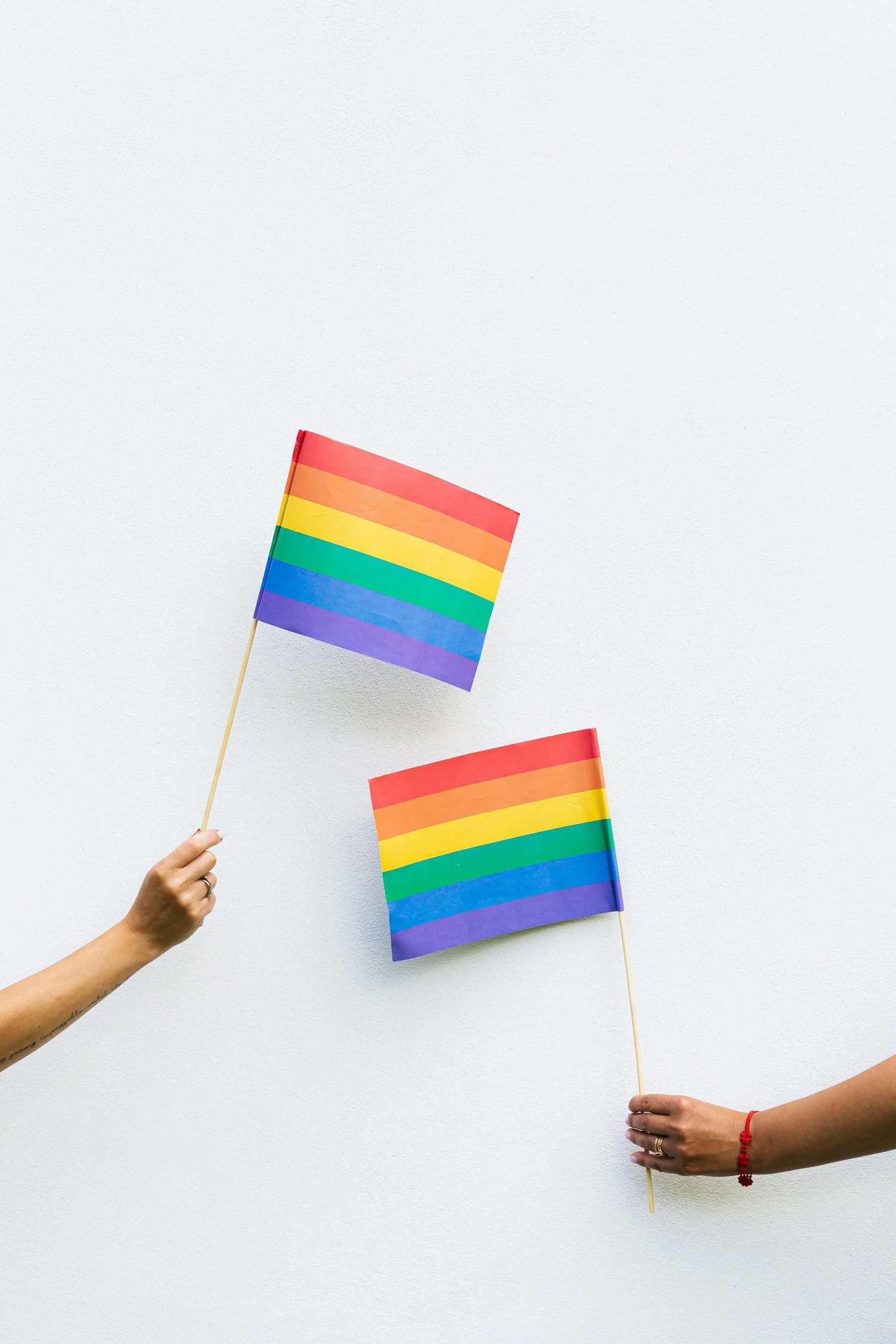 Two people holding rainbow Pride flags against a light wall.