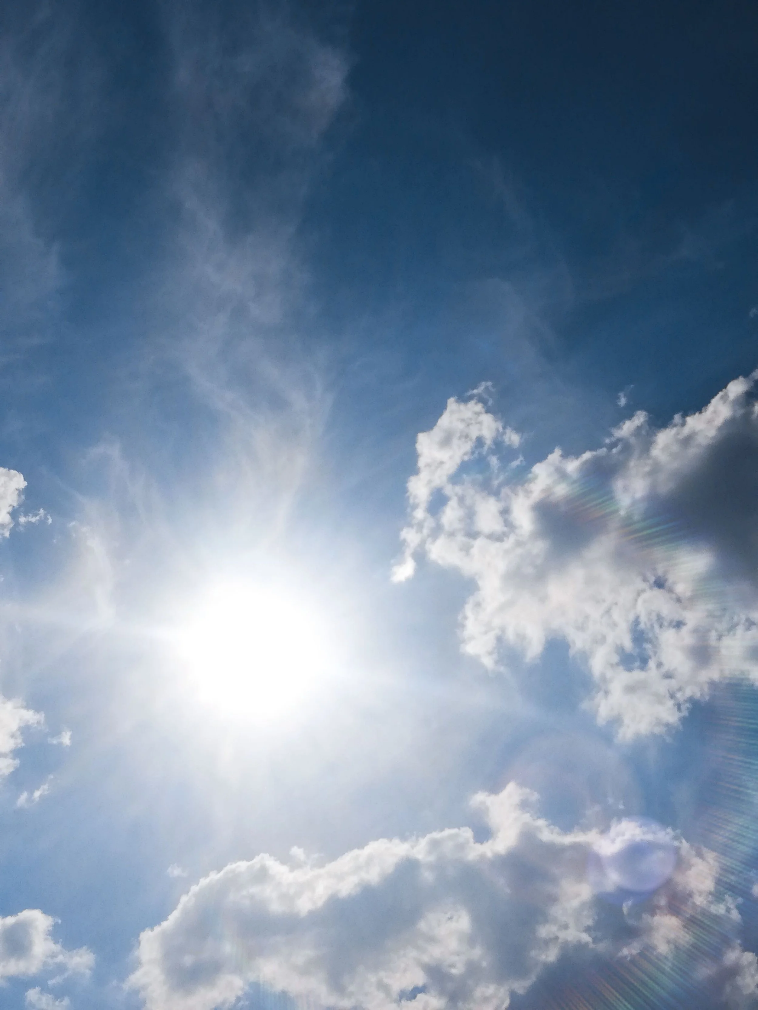 Sunlight shining through white clouds in a blue sky.