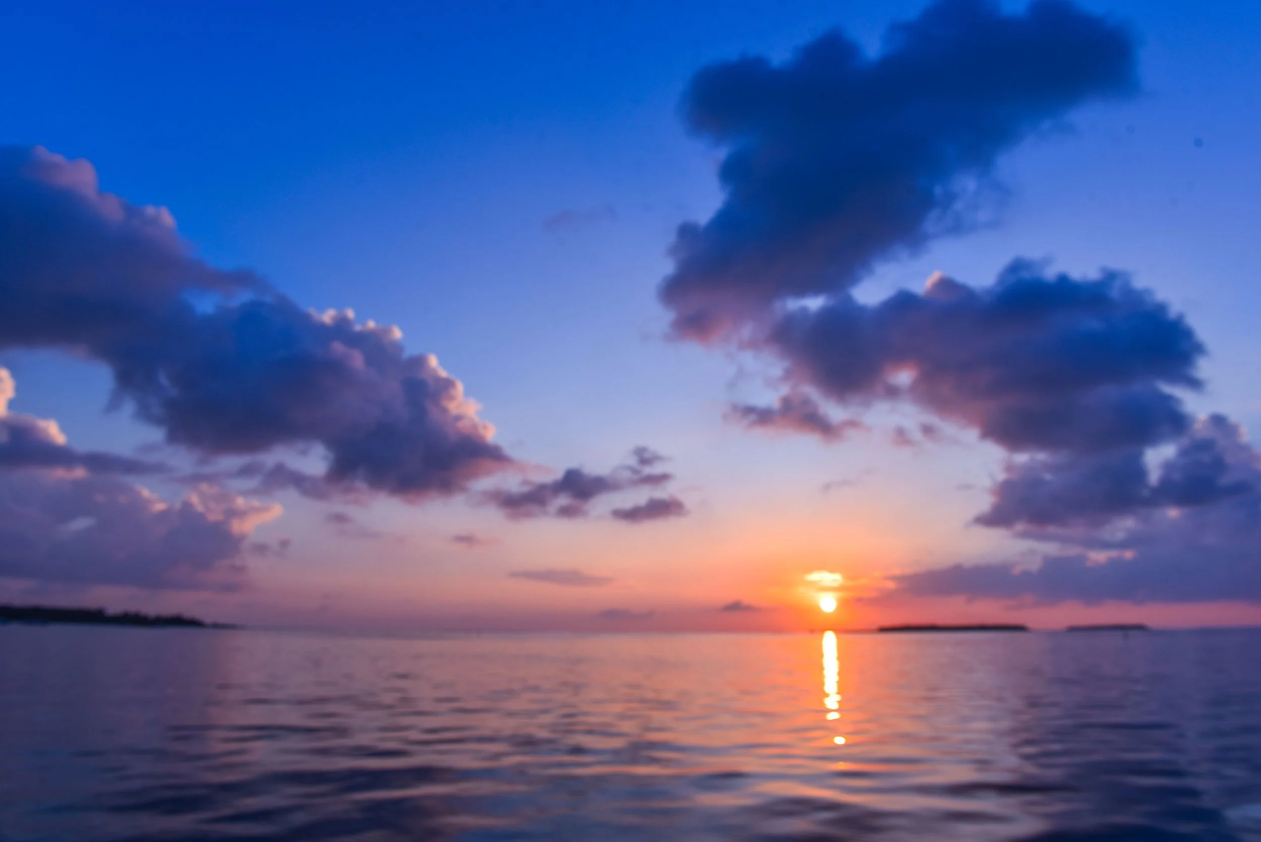 Sunset over calm water beneath colorful clouds.