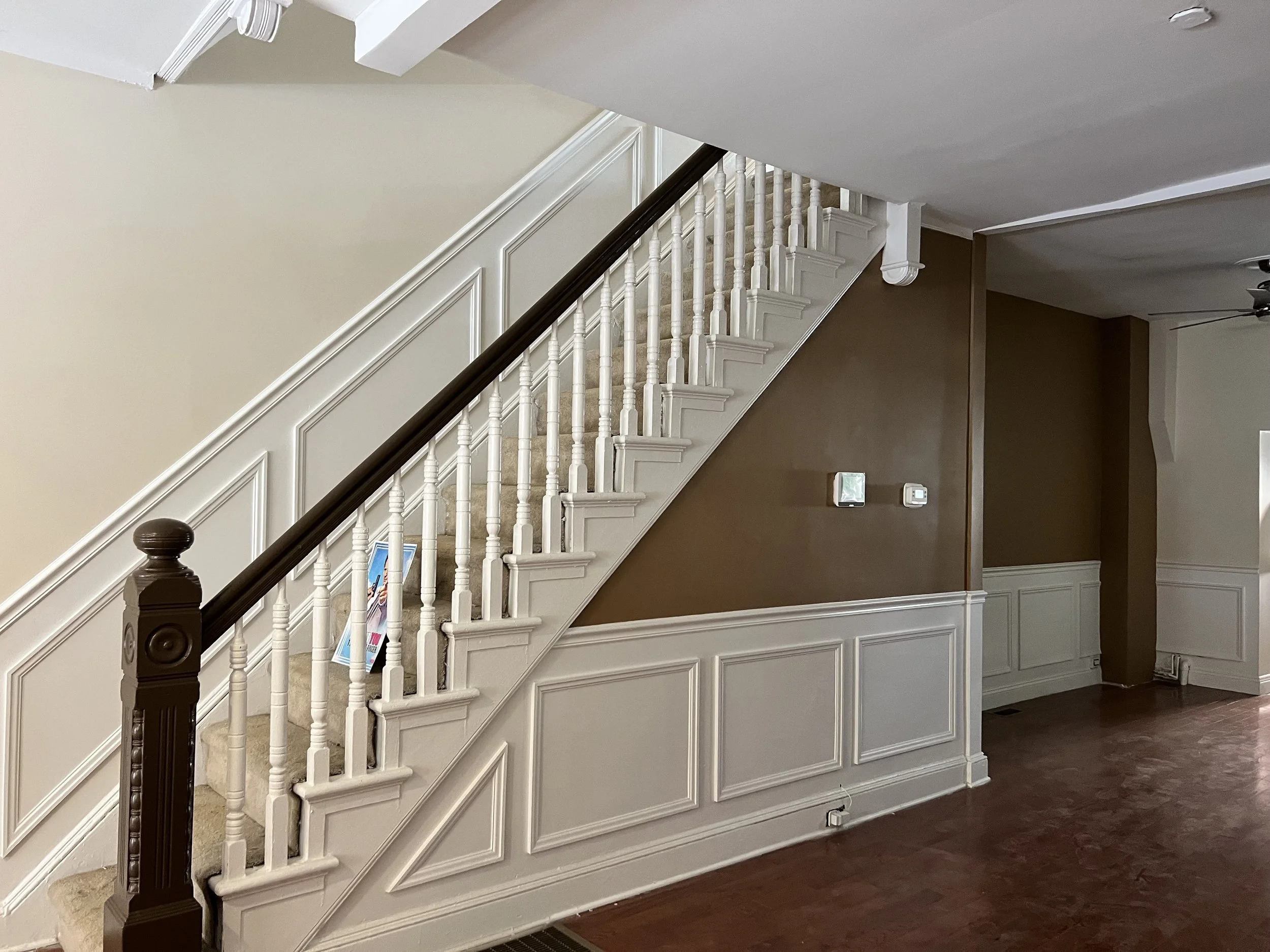 Interior view of a staircase with white railing and dark wood handrail, leading upstairs in a home with beige and brown walls and hardwood flooring.