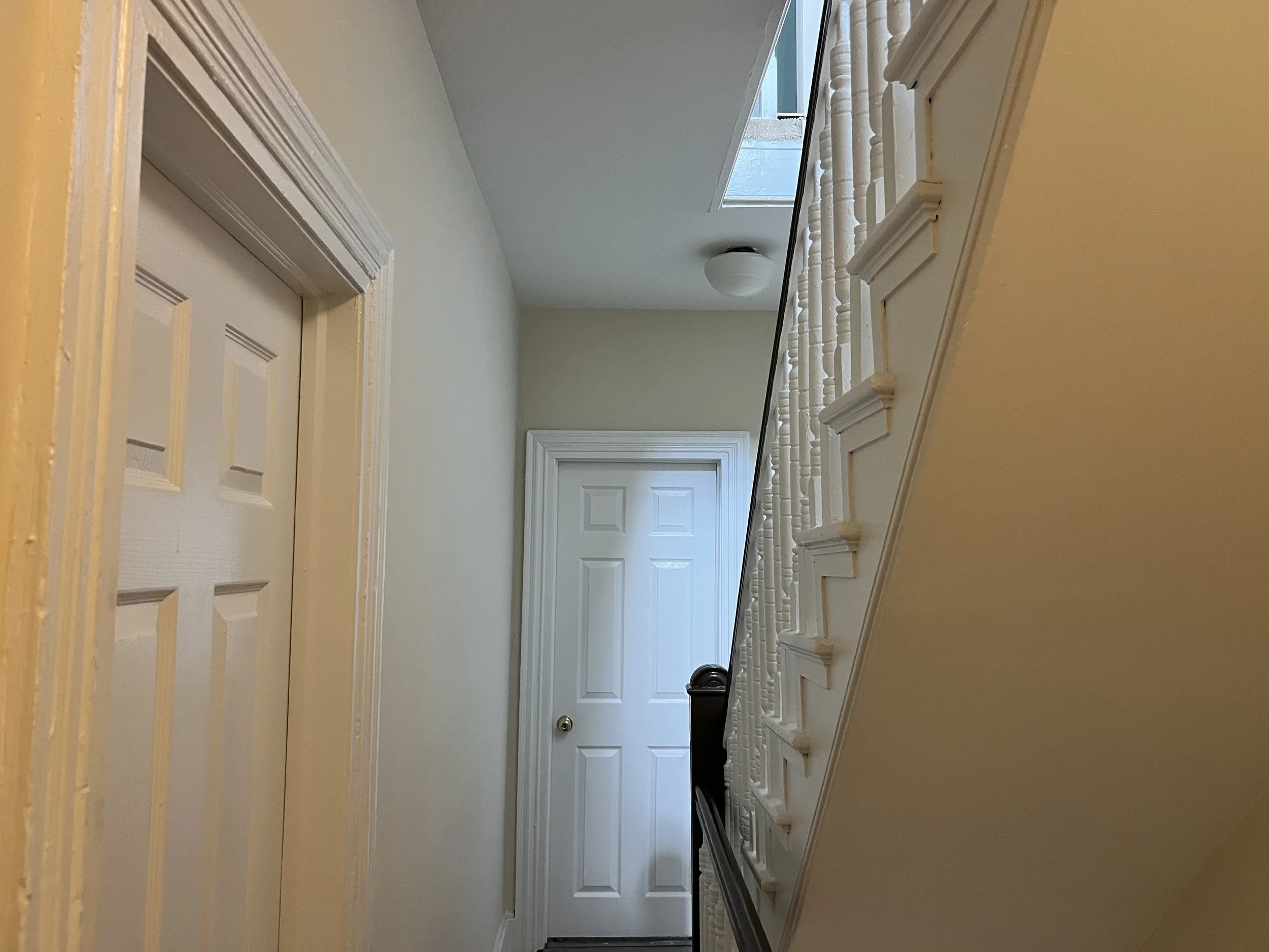 A residential hallway with white doors, beige walls, white staircase with wooden spindles, and a skylight.