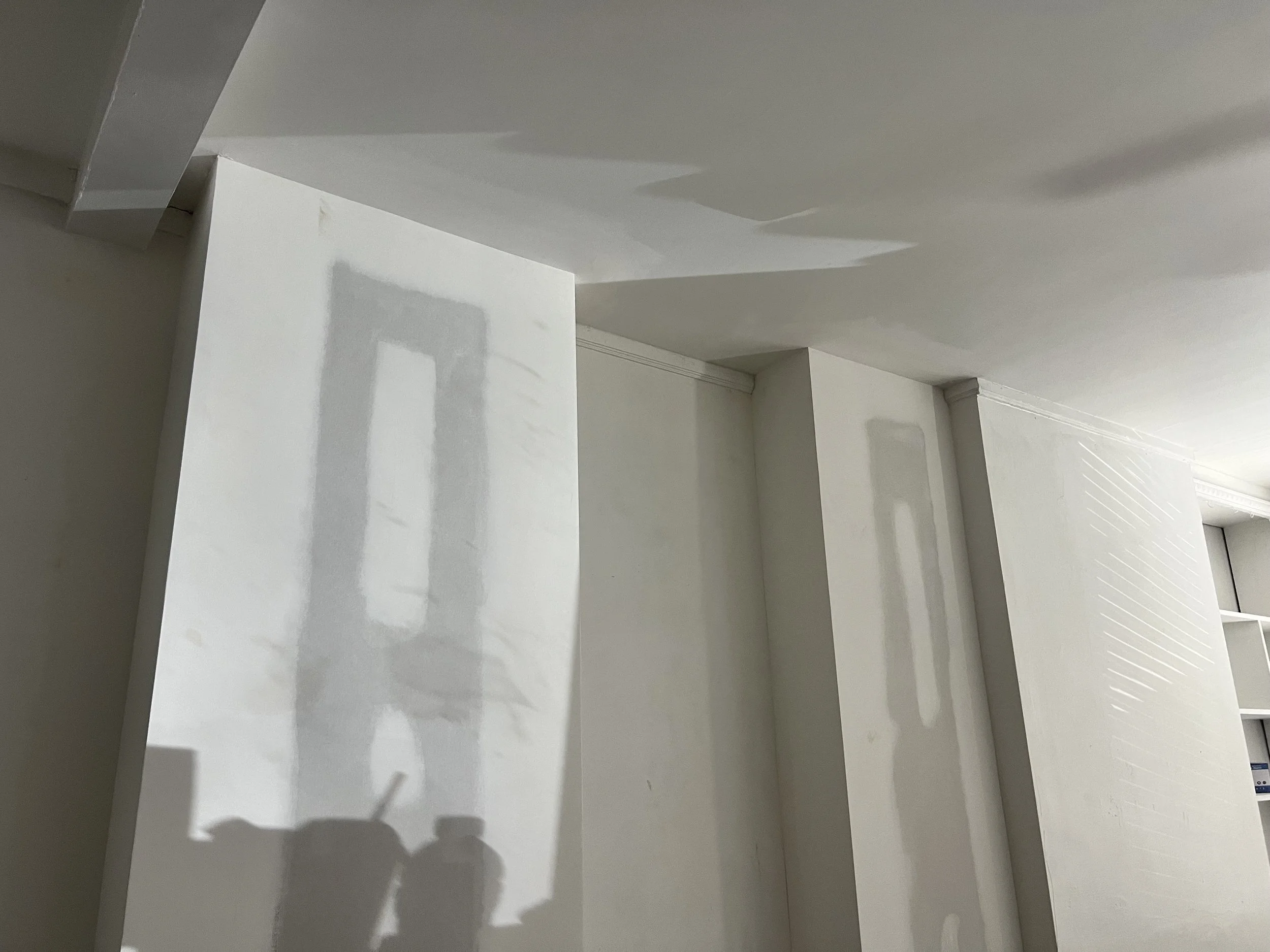 Interior view of white walls and ceiling with reflections and shadows, indicating ongoing painting or construction.