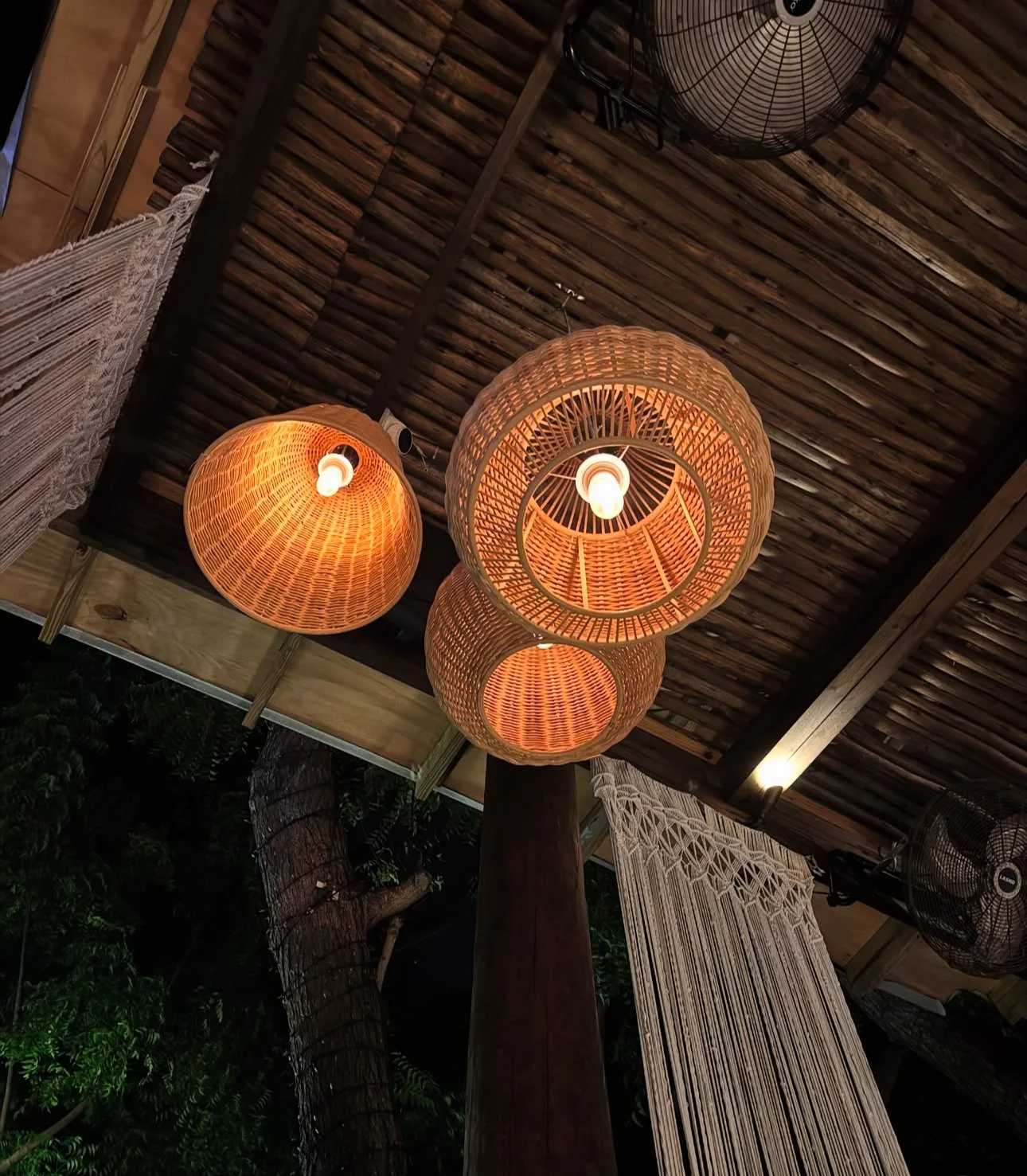 Three woven rattan pendant lights hanging from a wooden ceiling in a cozy indoor space.