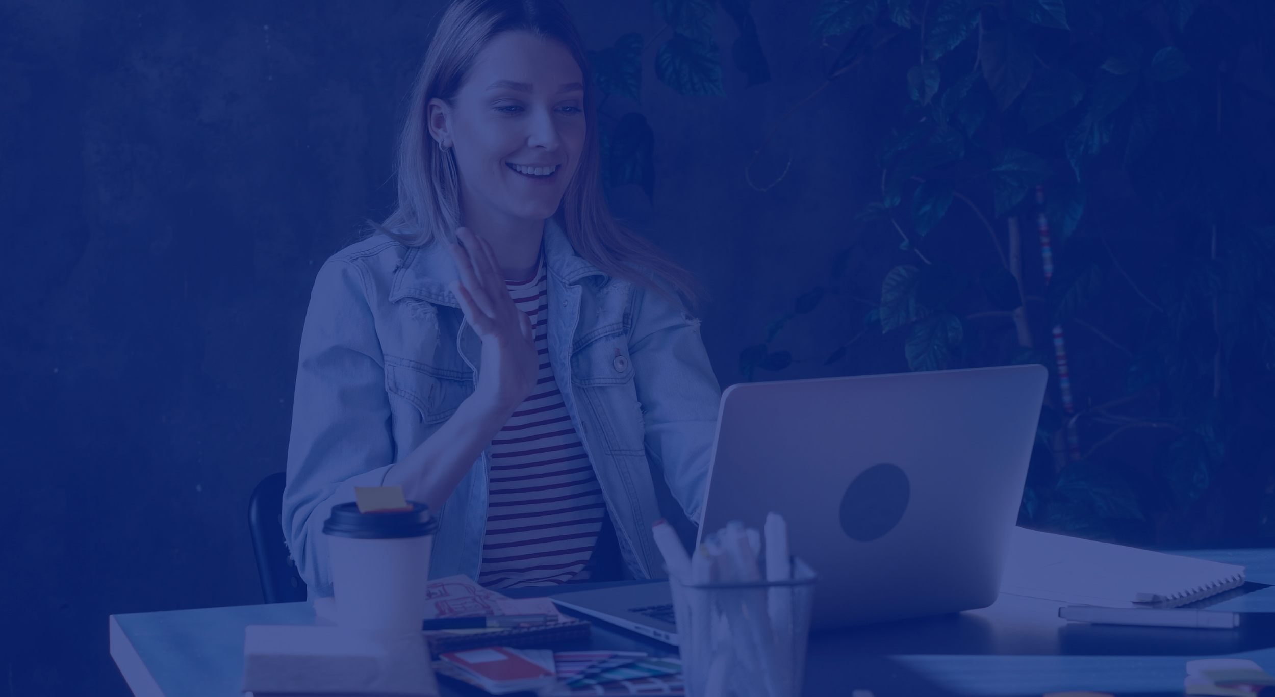 Joven mujer sonriendo usando una videollamada en una laptop en un ambiente interior con plantas.