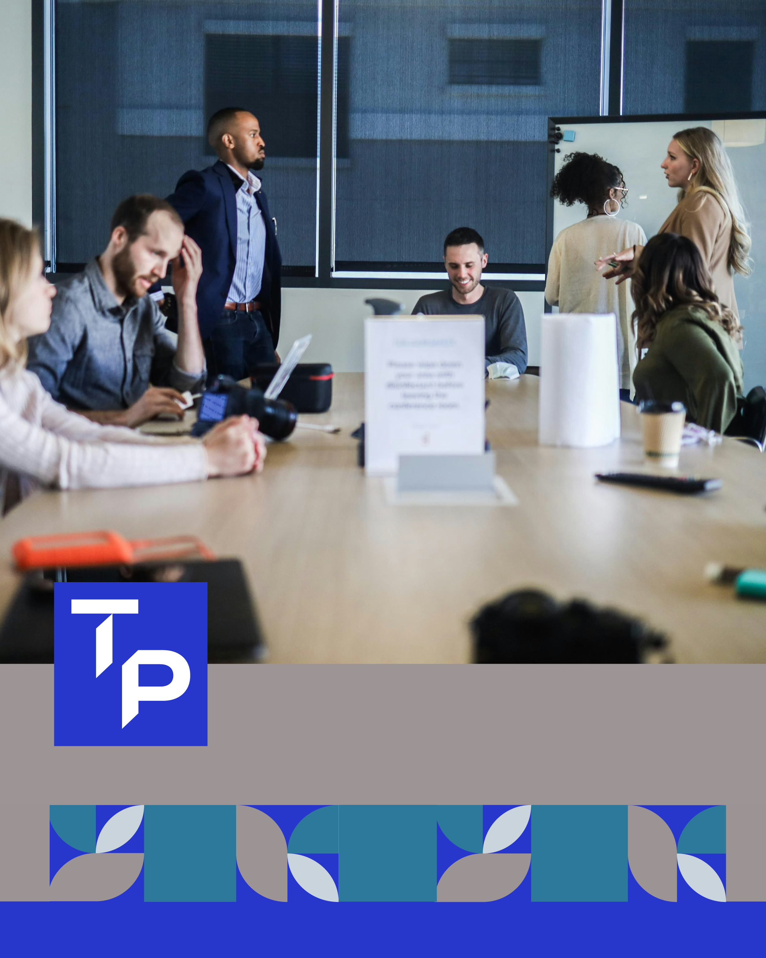 Grupo de personas en una reunión de trabajo en una sala de conferencias, con algunos usando computadoras portátiles y otros conversando.