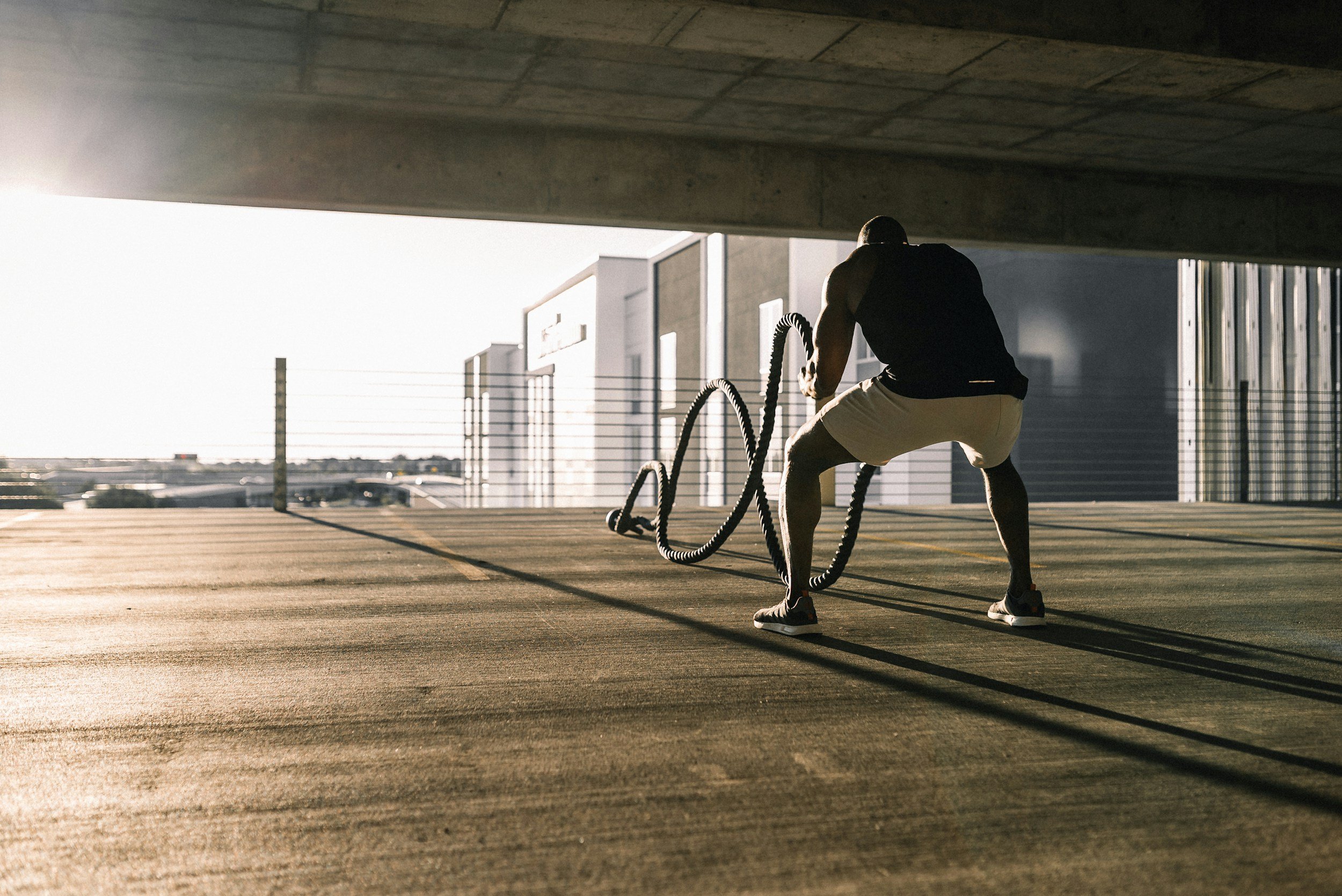 A man exercises with battle ropes under a concrete overpass during sunset.