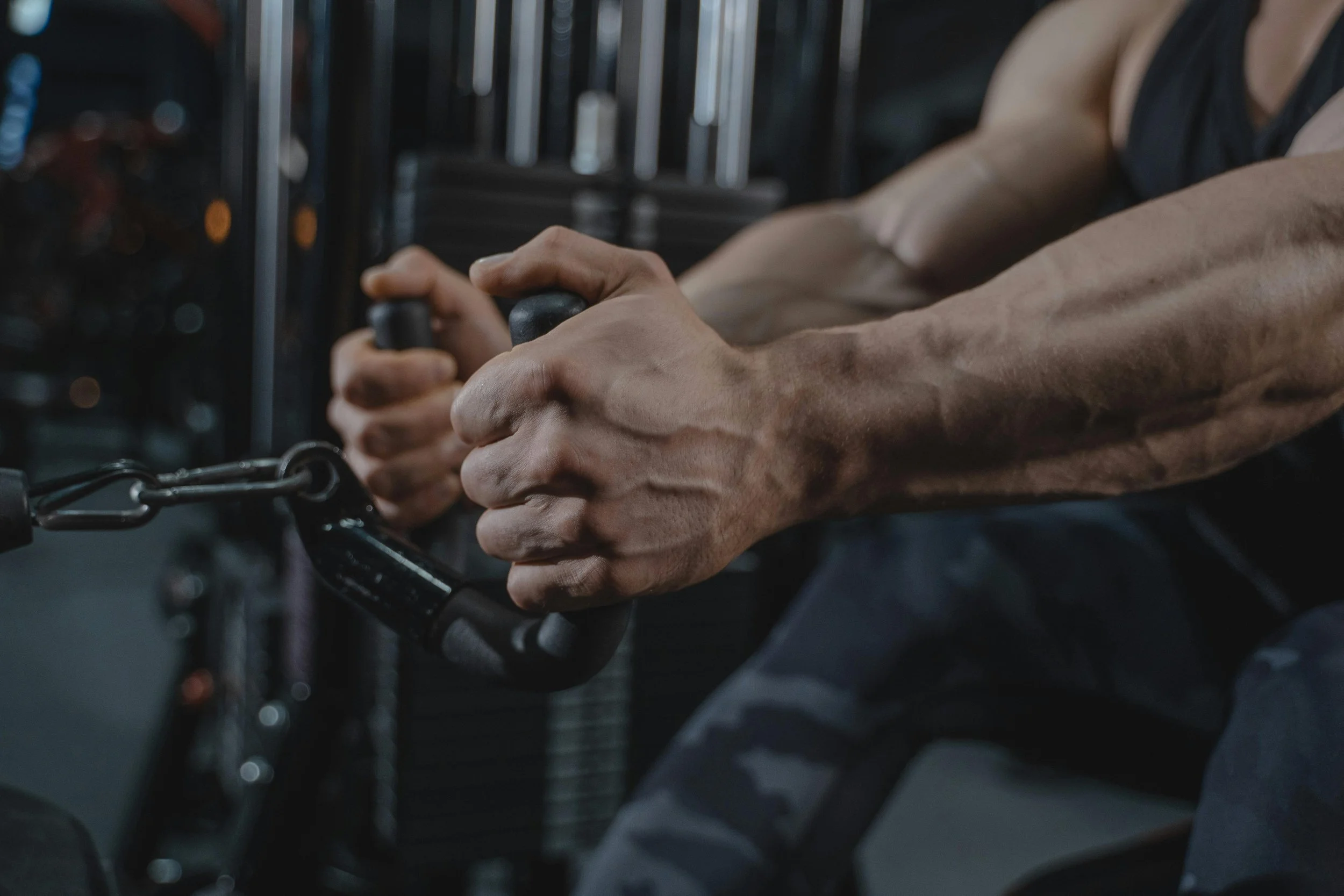 Close-up of muscular arms gripping handles on a cable machine in a gym.