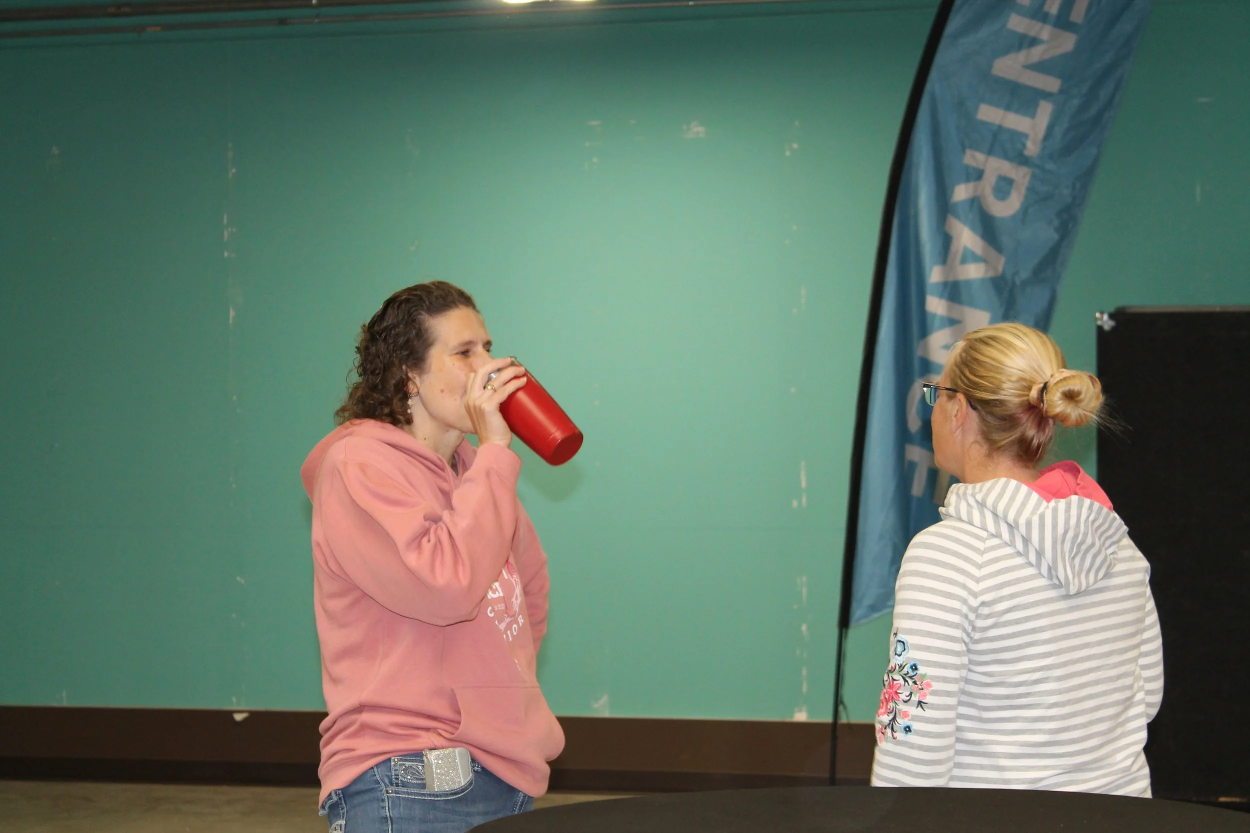 Two women in hoodies, one drinking from a red cup, the other facing away.