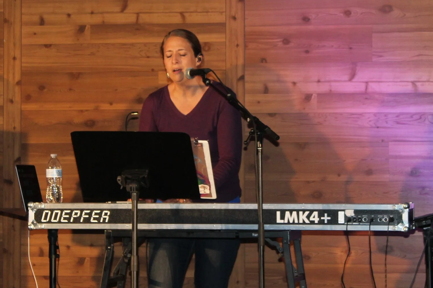 A woman singing into a microphone while playing a keyboard on a wooden stage.