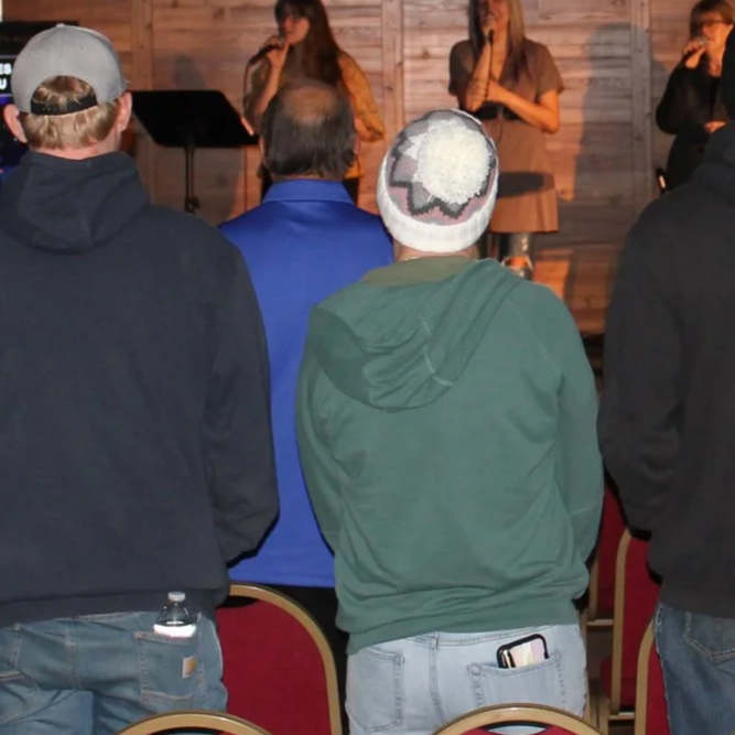 People standing and watching a musical performance on stage in an indoor venue with wooden walls.