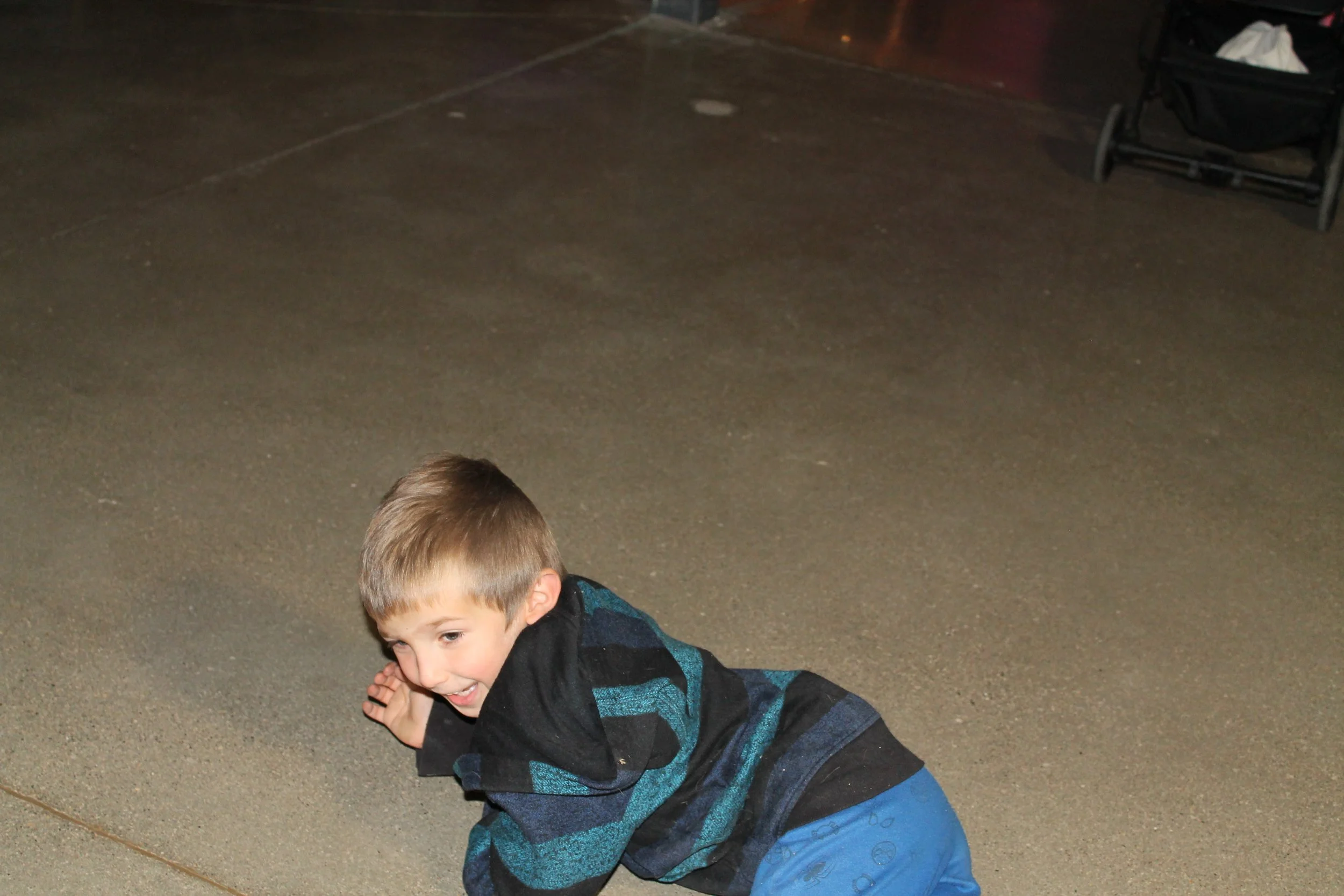Young boy lying on the ground, smiling, with an empty paved area and a stroller in the background.