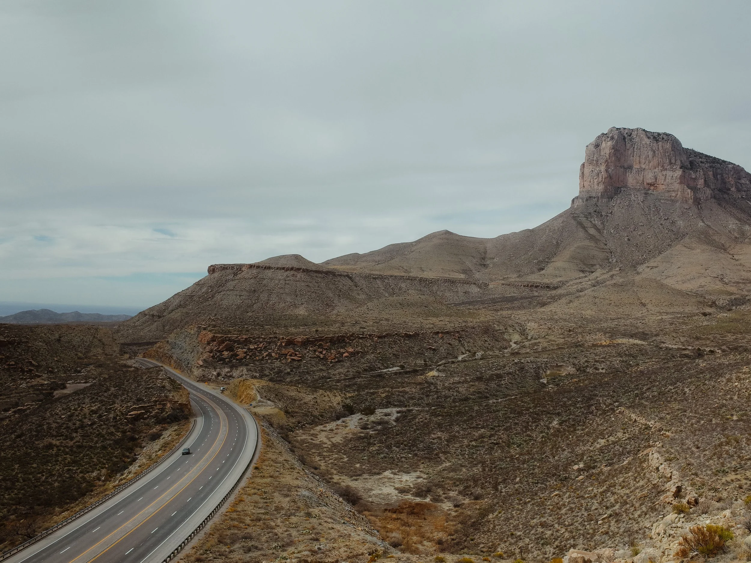 Desert landscape near Guadalupe Mountains National Park with a winding road and large rock formations under a cloudy sky.
