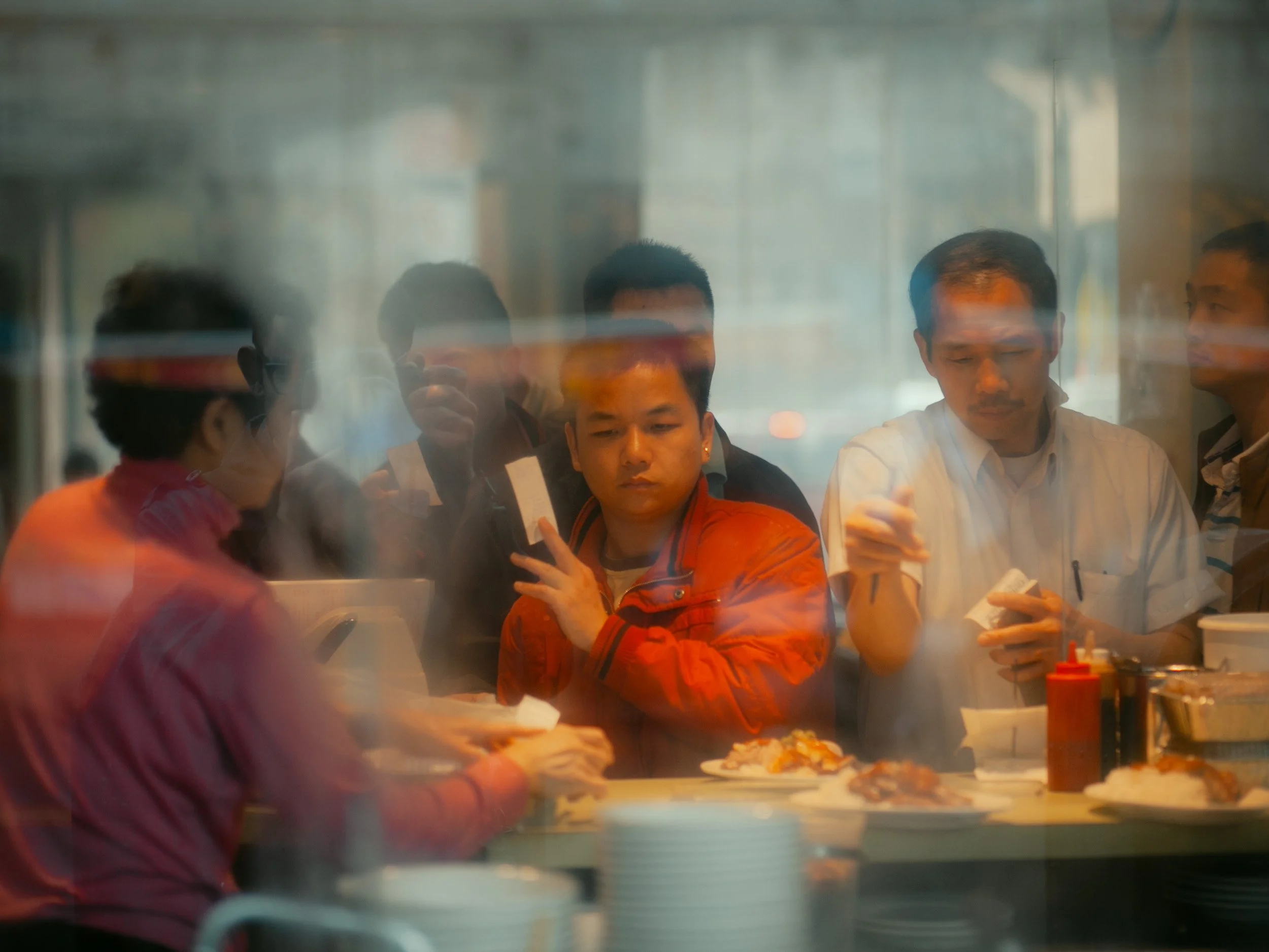 People dining at a restaurant, seen through a foggy glass window, eating and chatting.