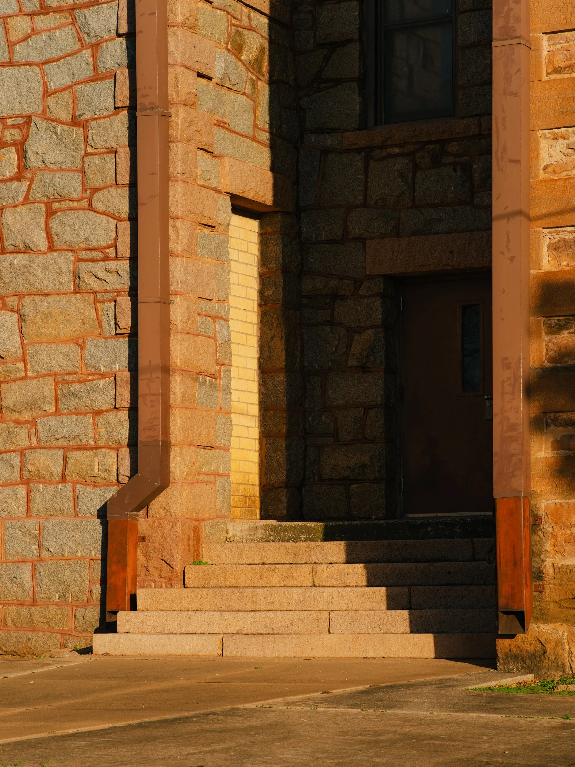 Stone building entrance with three steps, brown drainpipes, and a dark door.