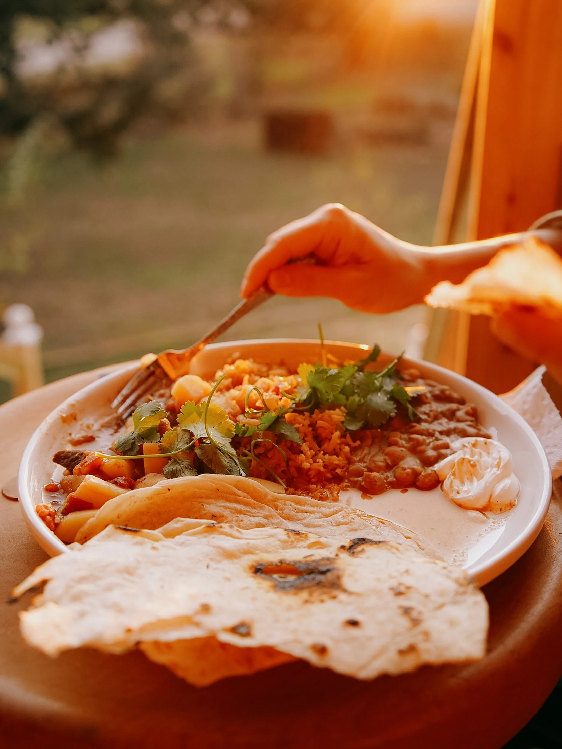 A plate of Mexican food with beans, rice, cilantro, sour cream, and a piece of tortilla on a wooden table.